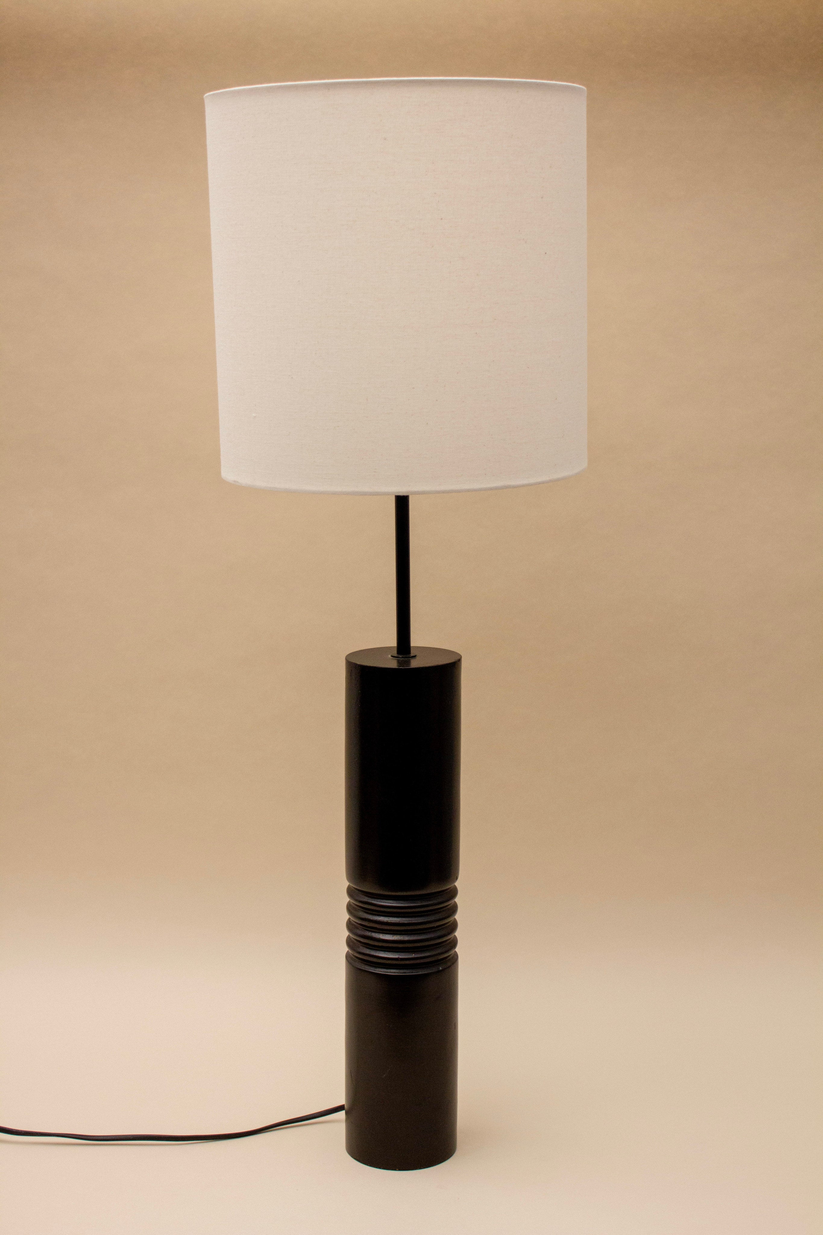 The SÒLER SALAMANQUE TABLE LAMP features a black wooden base with ridged detailing and a simple white shade, shown against a plain beige background.