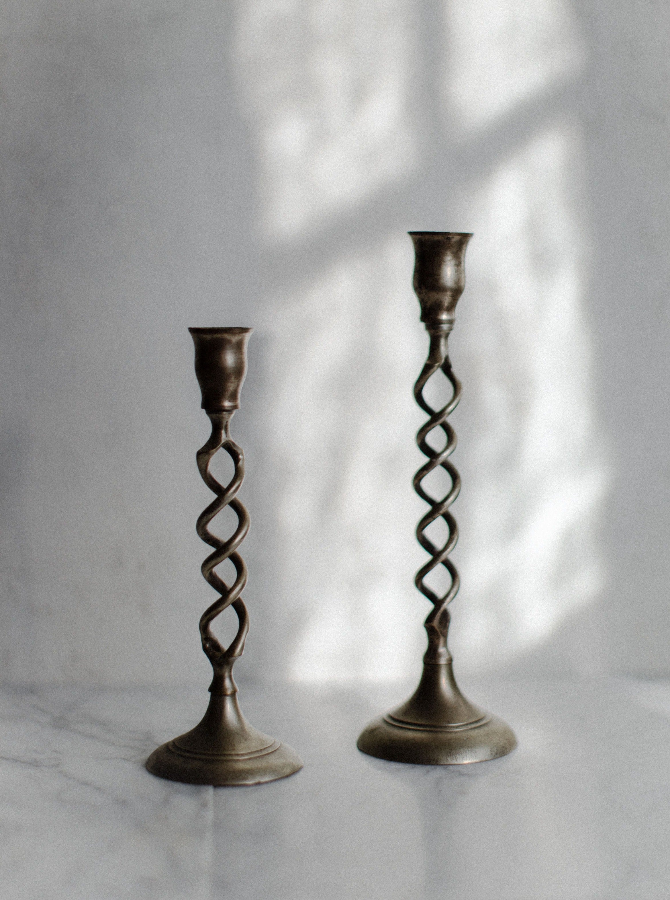 Two Out For Lunch Brass Twisted Candleholders on a marble surface, with a soft shadow pattern on the wall behind them.