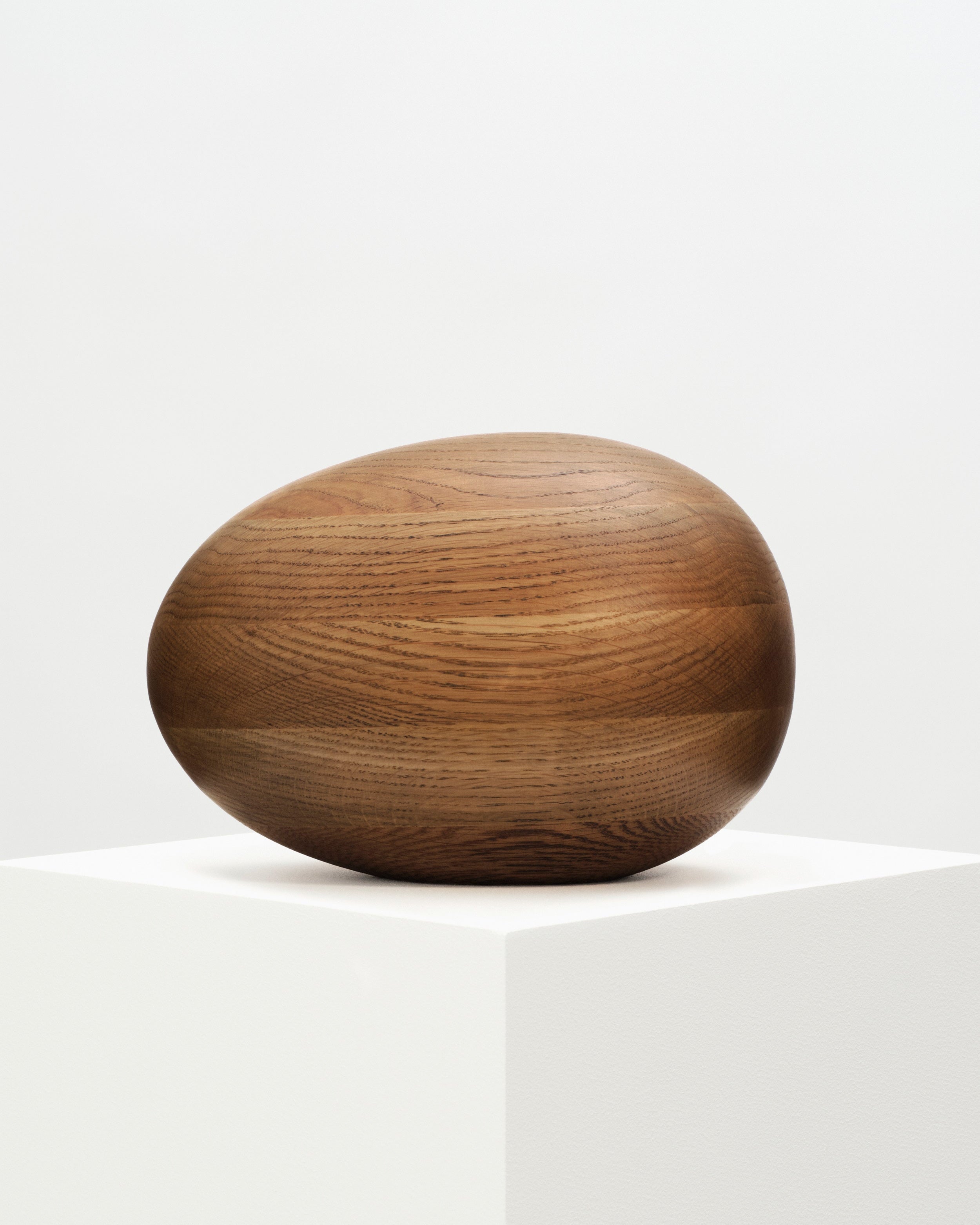 Smoked Oak Egg Sculpture resting on a wooden pedestal, showing intricate details and smooth texture