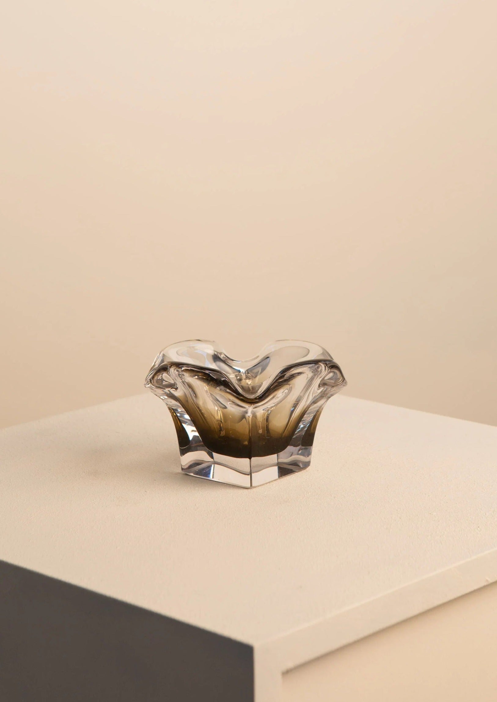 A handcrafted Treaptyque Murano Flower Vide Poche with a wavy, flower-like design resting on a gray platform against a soft beige background.