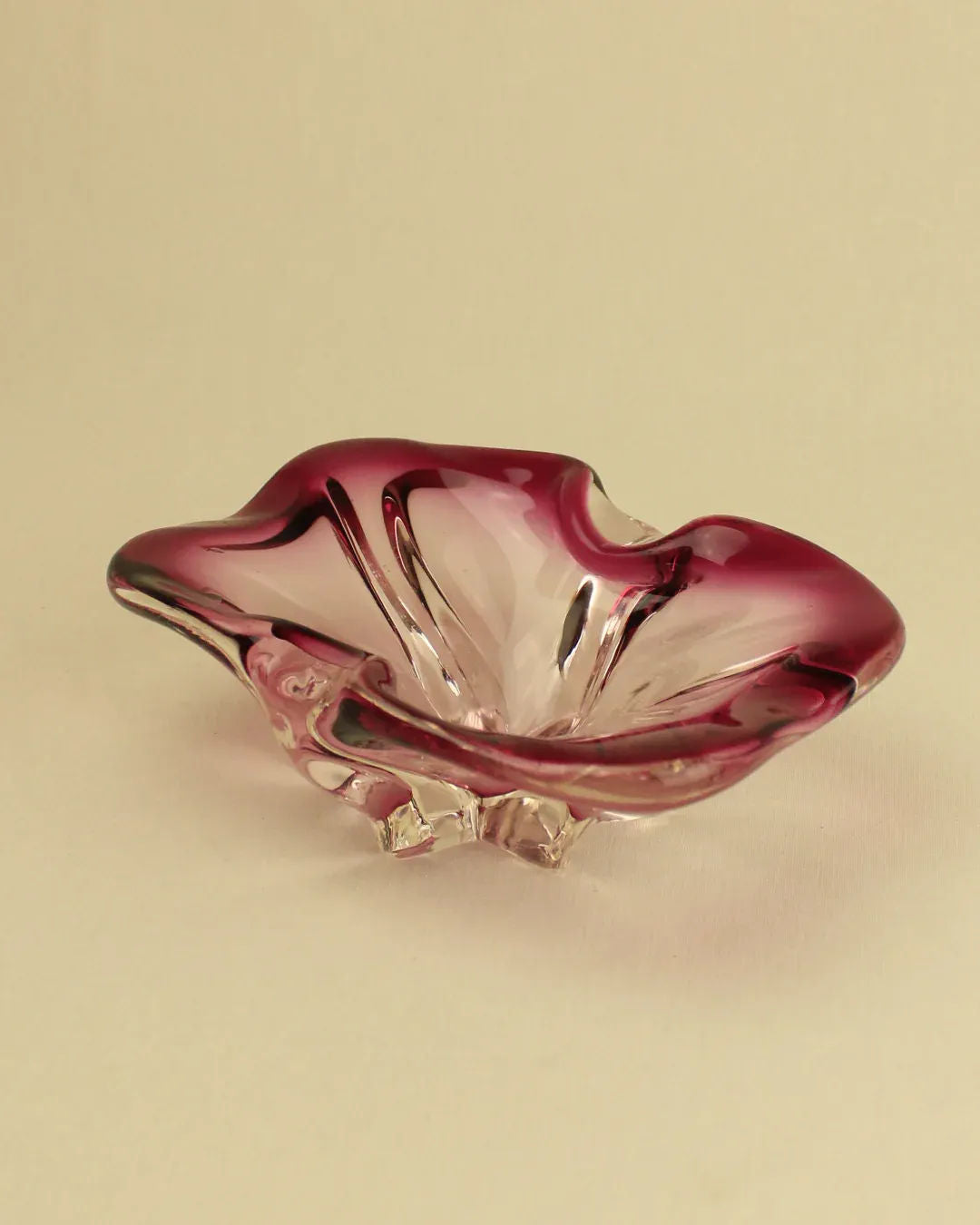 A delicate Boga Avante Shop Murano Bowl shaped like a flower with pink and clear coloration, resting on a neutral background.