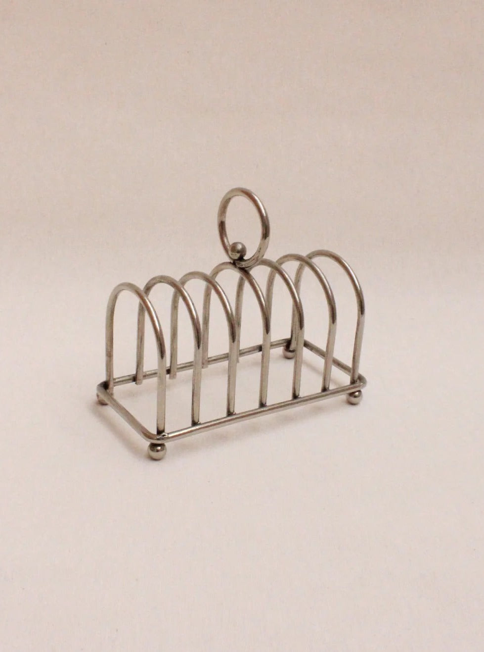 A vintage Boga Avante Shop Art Deco toast rack with curved slots and a circular handle on a beige background.