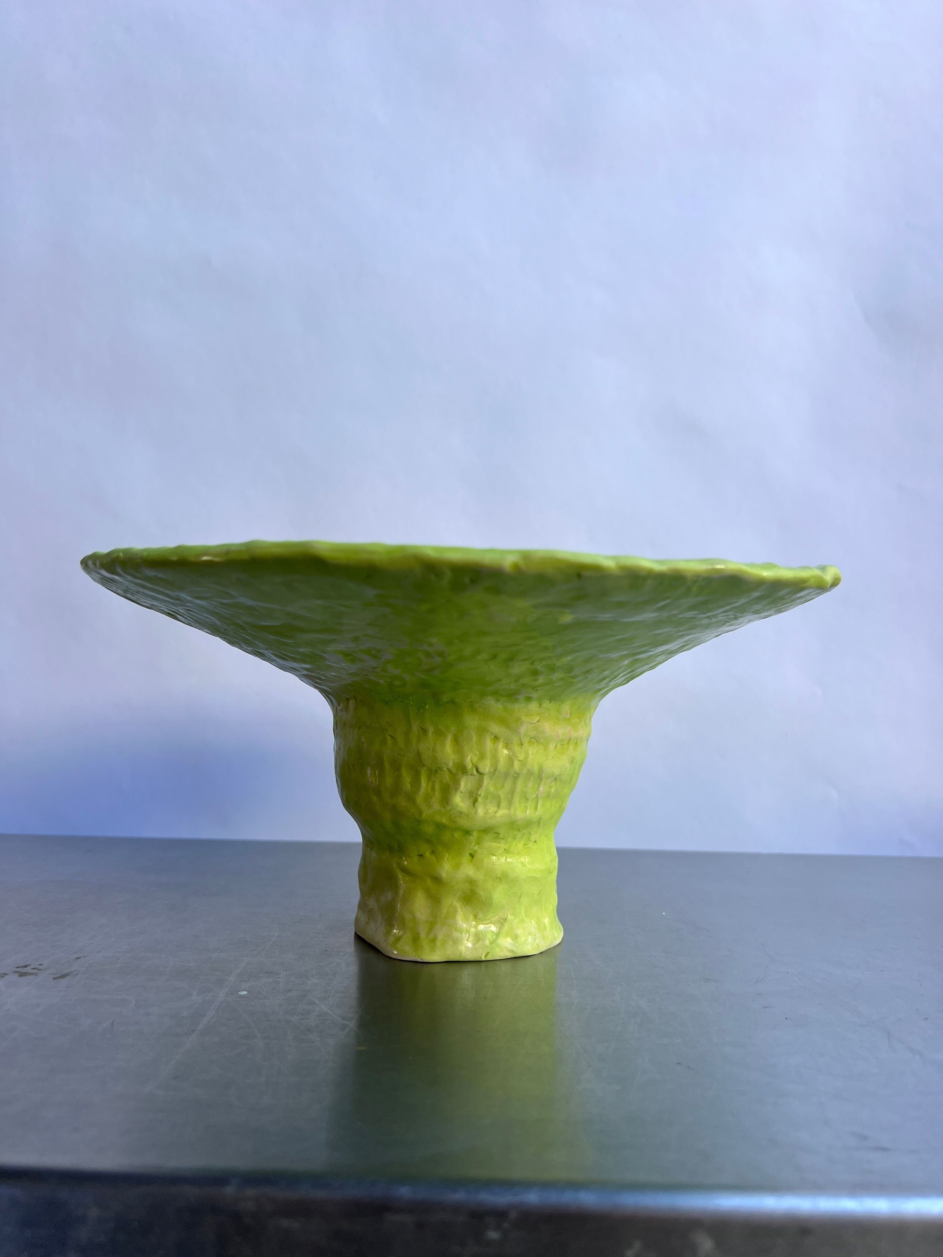 A vivid lime, matte-glazed ceramic Pistil Fruit Basket - Large with a wide, flared rim and a narrow base, displayed against a plain light blue background by burrata studio.