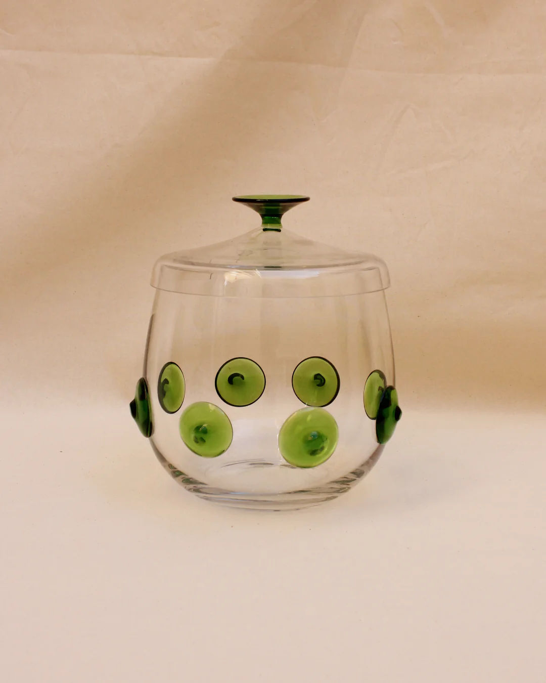 A Murano Punch Bowl from Boga Avante Shop, adorned with green circular patterns and dots, featuring a matching green lid, displayed on a beige background as a centerpiece.