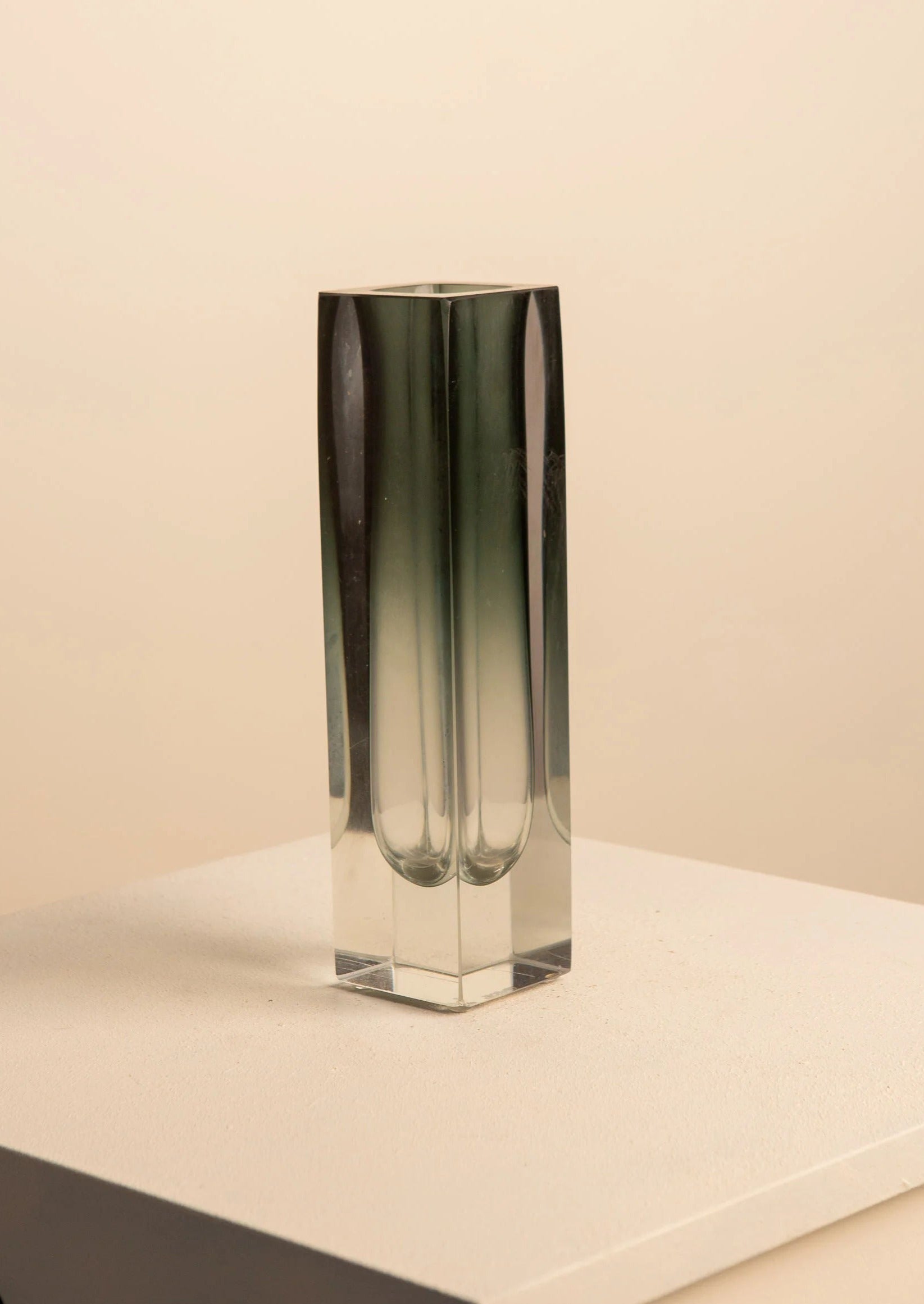 The Black Vase by Flavio Poli for Seguso, from Treaptyque, is a tall, slender rectangular glass piece with a gradient design. It elegantly stands on a light-colored surface against a beige background, exemplifying minimalist aesthetics and handcrafted elegance.