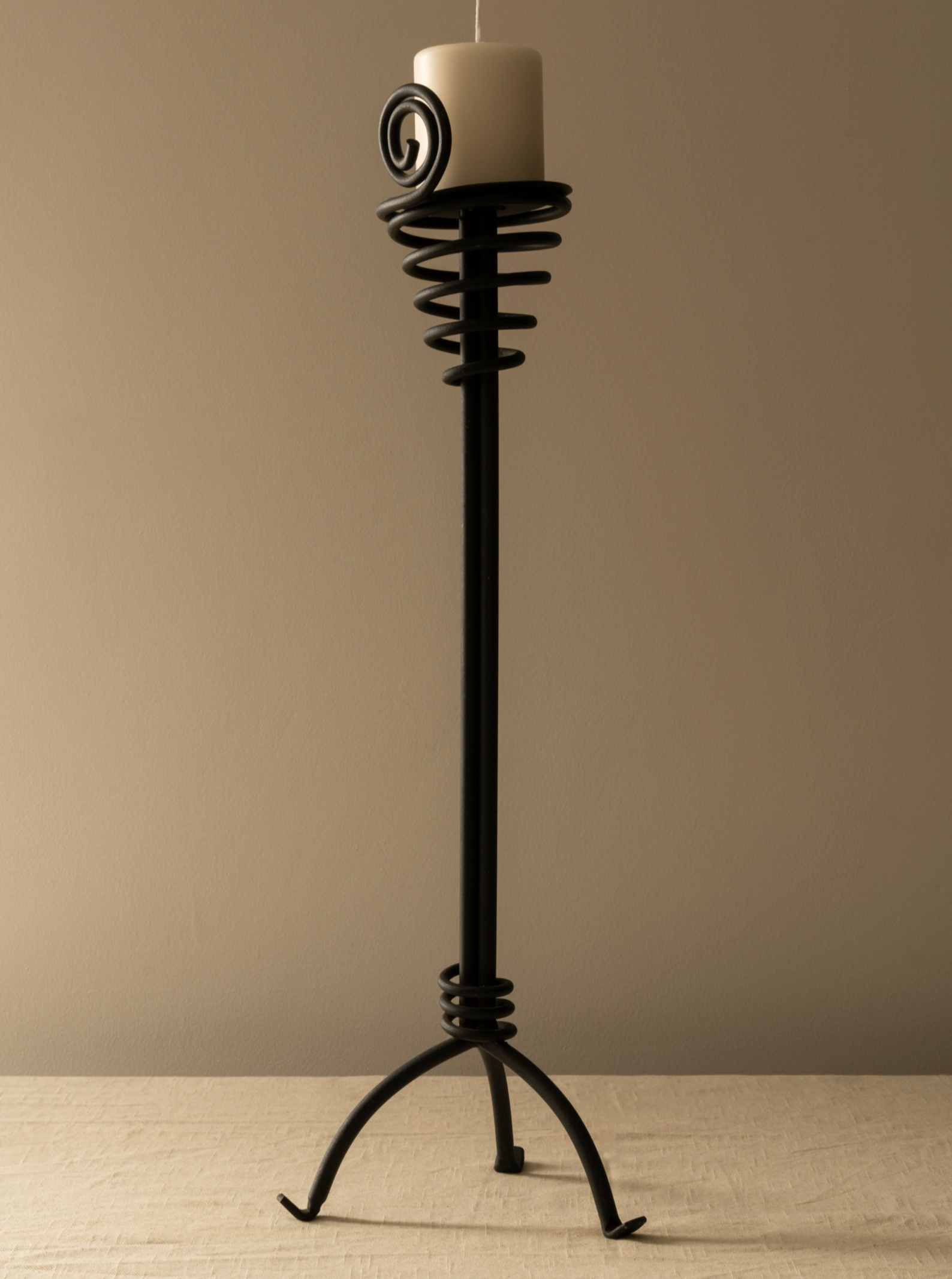 A tall, Les Objets Amsterdam candle holder with a spiral design and a circular base, supporting a white pillar candle on a neutral background.