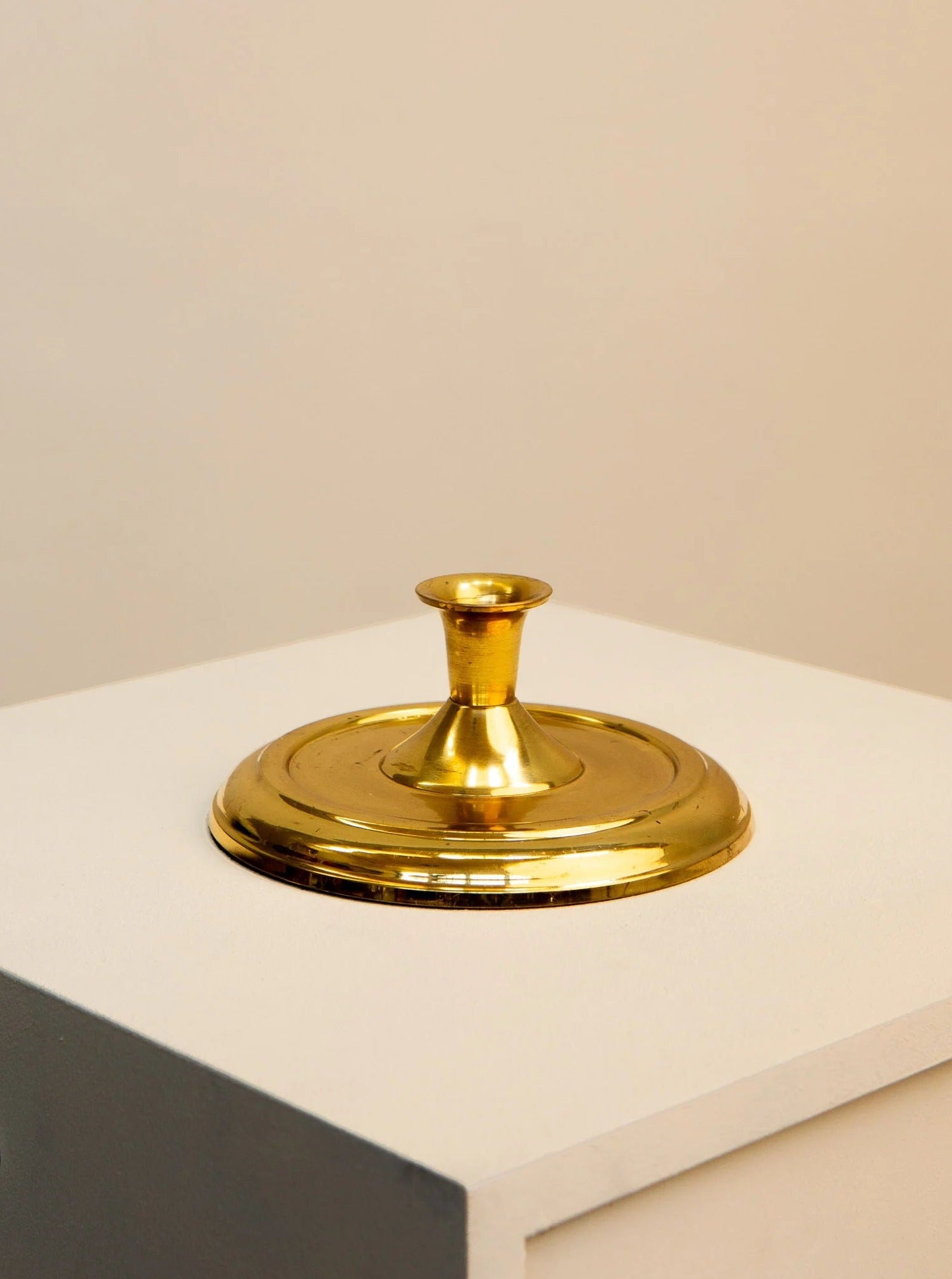 A Treaptyque 60's Circular Candlestick in Gilded Metal, with a decorative accent, placed on top of a white pedestal against a soft beige background.