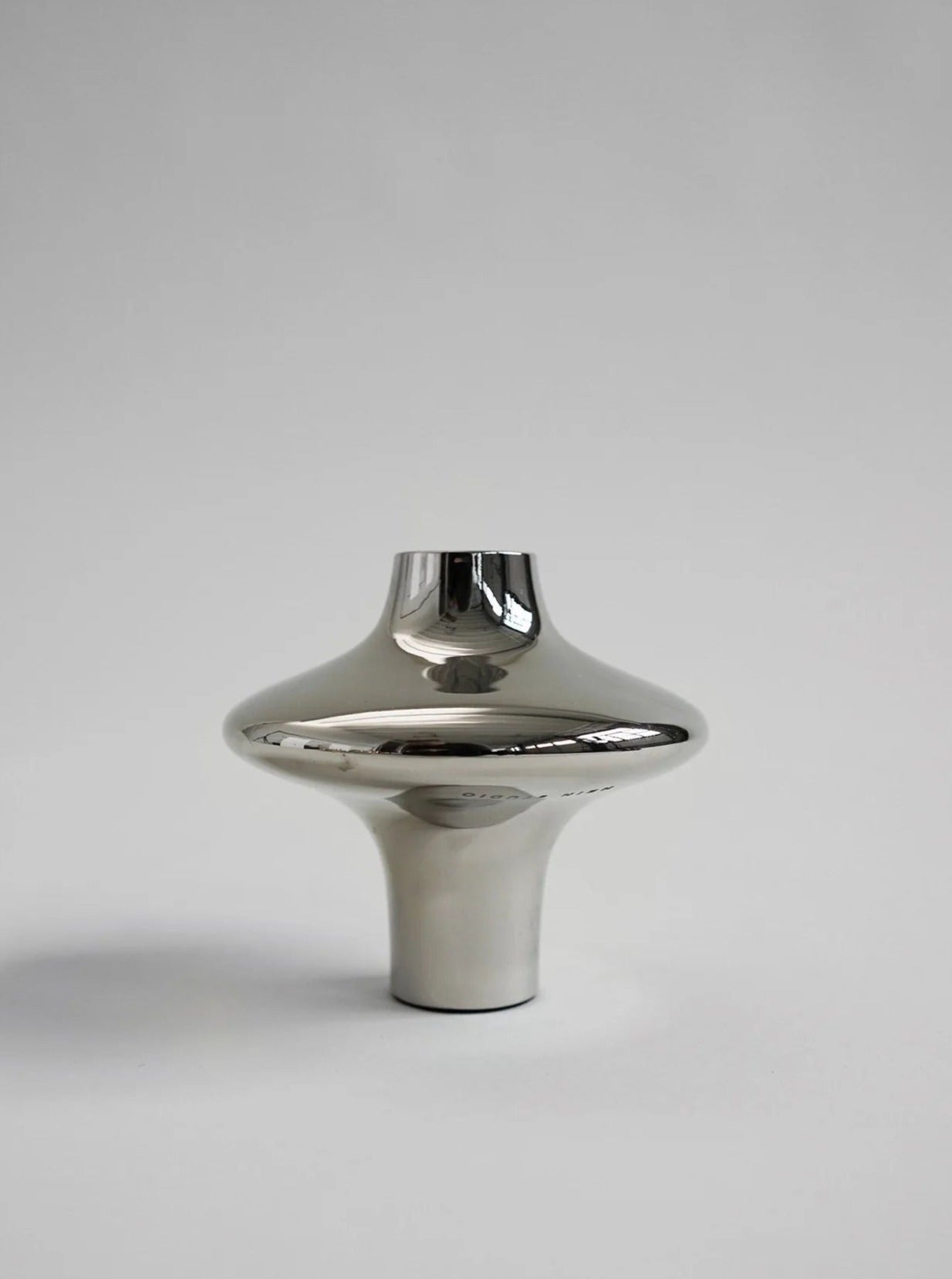 The Doublet Candleholder - Large - Silver from Hein Studio features a sleek, reflective metallic finish with a wide, rounded body and narrow base and top. This elegant piece embodies contemporary design with sculptural curves, perfect for enhancing luxury interiors against its light gray background.