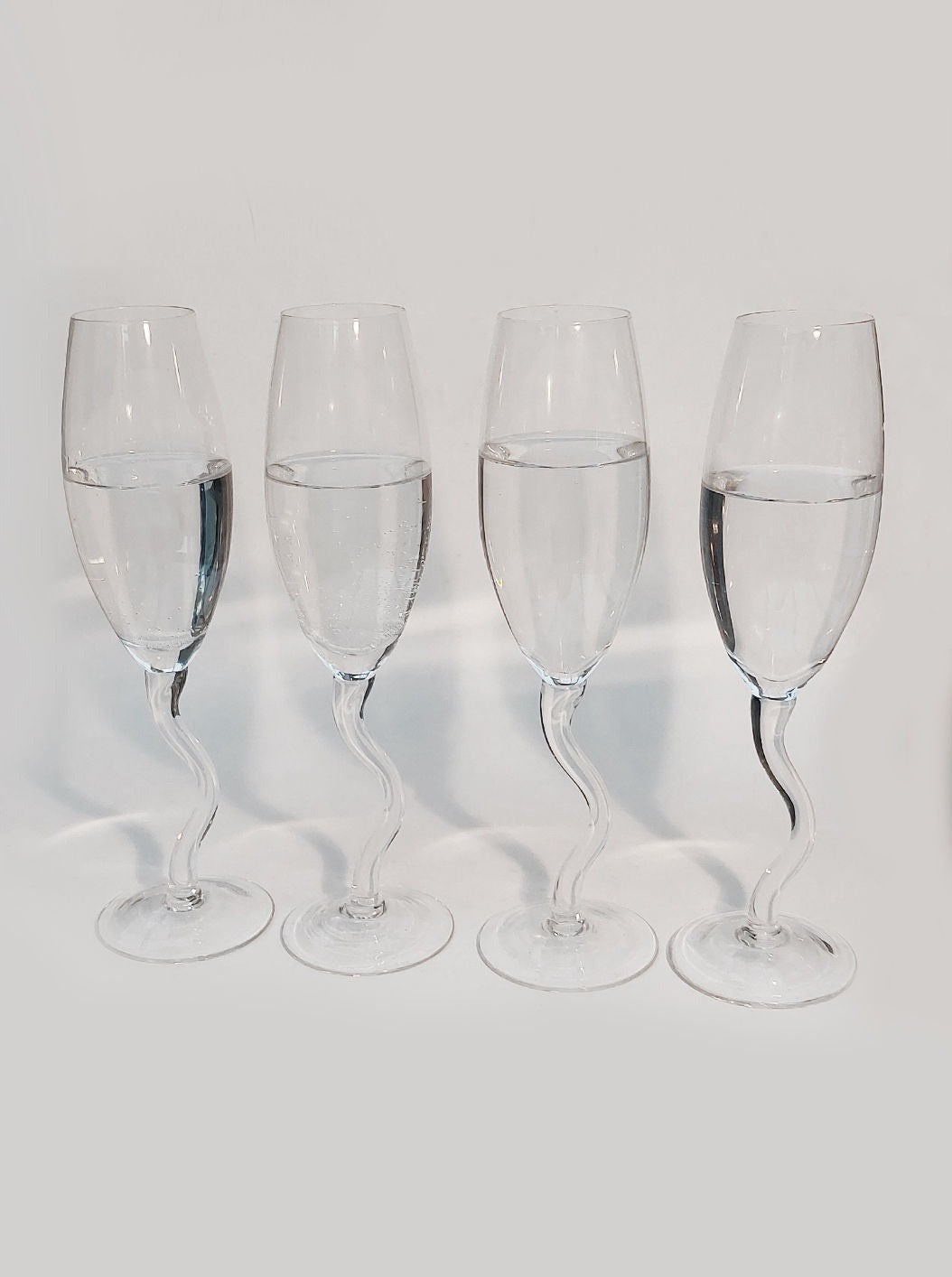 Four Zig Zag Champagne Flutes of varying water levels arranged in a set of 4 on a white background, showcasing differences in tilt and liquid displacement by Les Objoies.