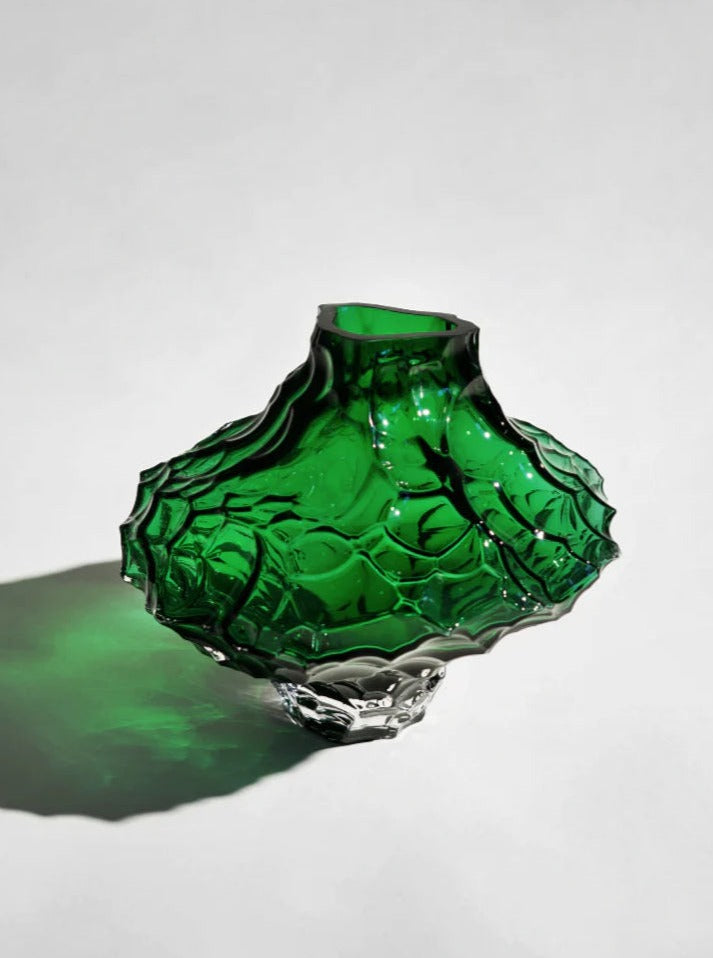 A vibrant green, irregularly shaped Hein Studio Canyon Vase with intricate textures, casting a vivid green shadow on a white surface.