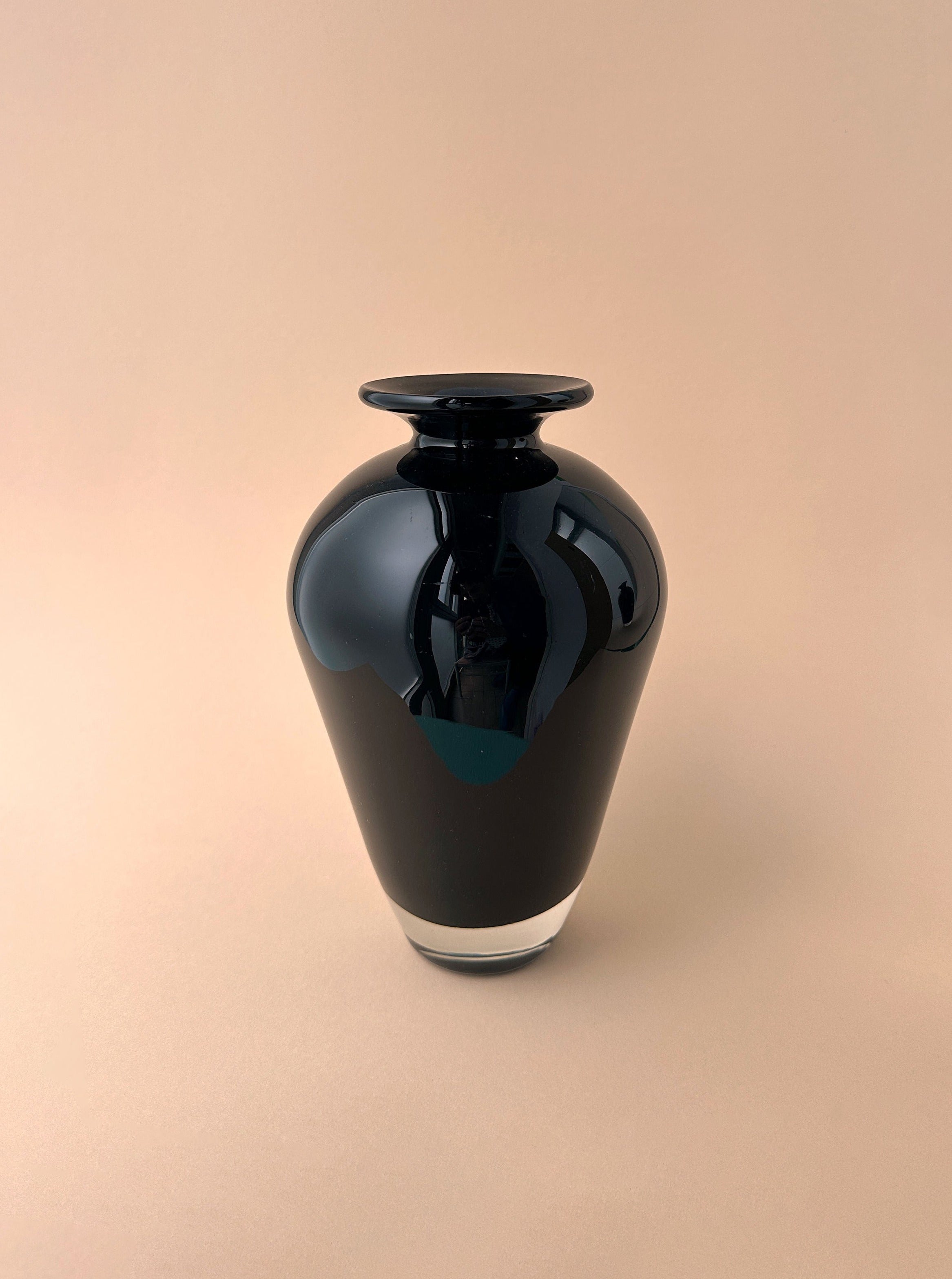 A sleek, black 1950s Black Murano Vase by Paolo Venini with a reflective surface and a narrow neck, set against a soft beige background.
