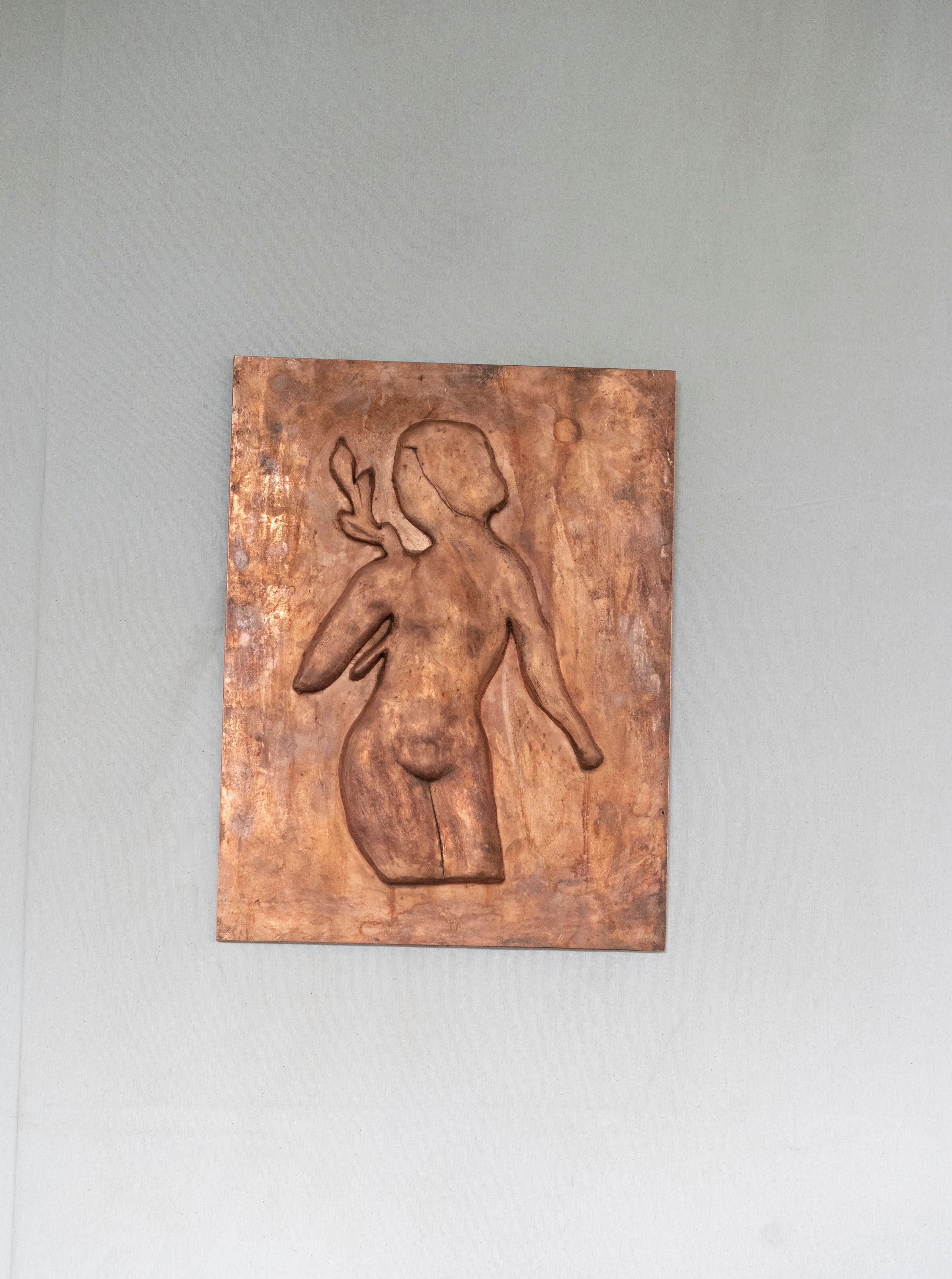 A Woman with Laurel leaves Chikanka bas-relief sculpture of a stylized human figure mounted on a gray wall. The figure appears abstract and is depicted in a gestural pose with a raised arm by Rooms Studio.