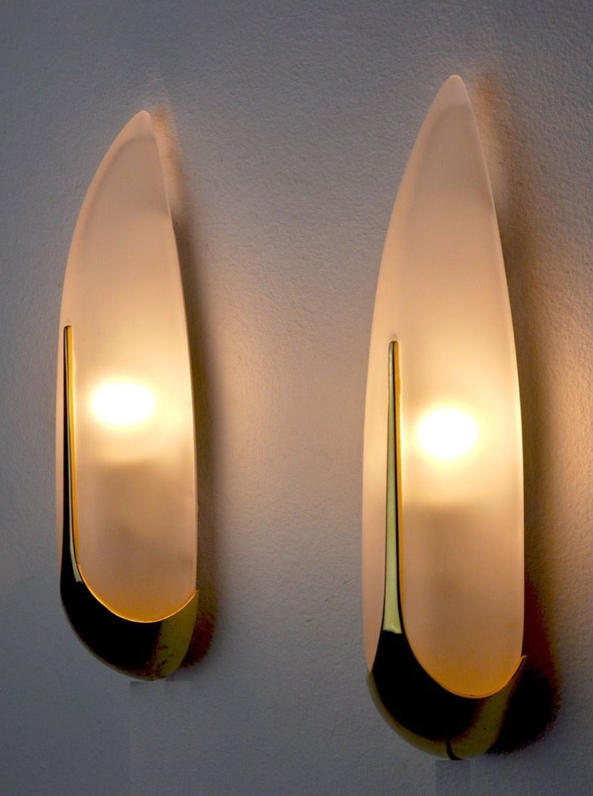 Two Pair of "ears of corn" Sconces by Idearte 1980 with a sleek design, featuring smoked glass and emitting a warm, soft glow on a light-colored wall.