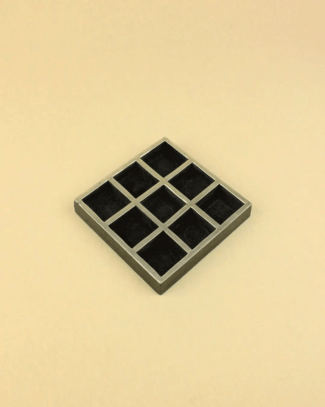 A square-shaped, gray tray resembling a Vintage Tic Tac Toe Game with nine black compartments, viewed from above against a plain, light beige background by Boga Avante Shop.