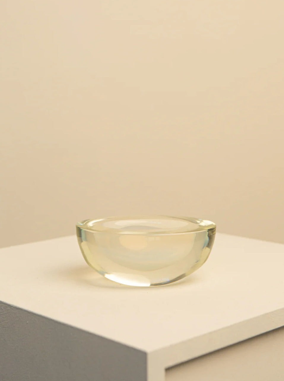 A 70's Oval Murano Glass Vide Poche by Treaptyque containing water is centered on a light gray tabletop against a beige background, emphasizing simplicity and minimalism.