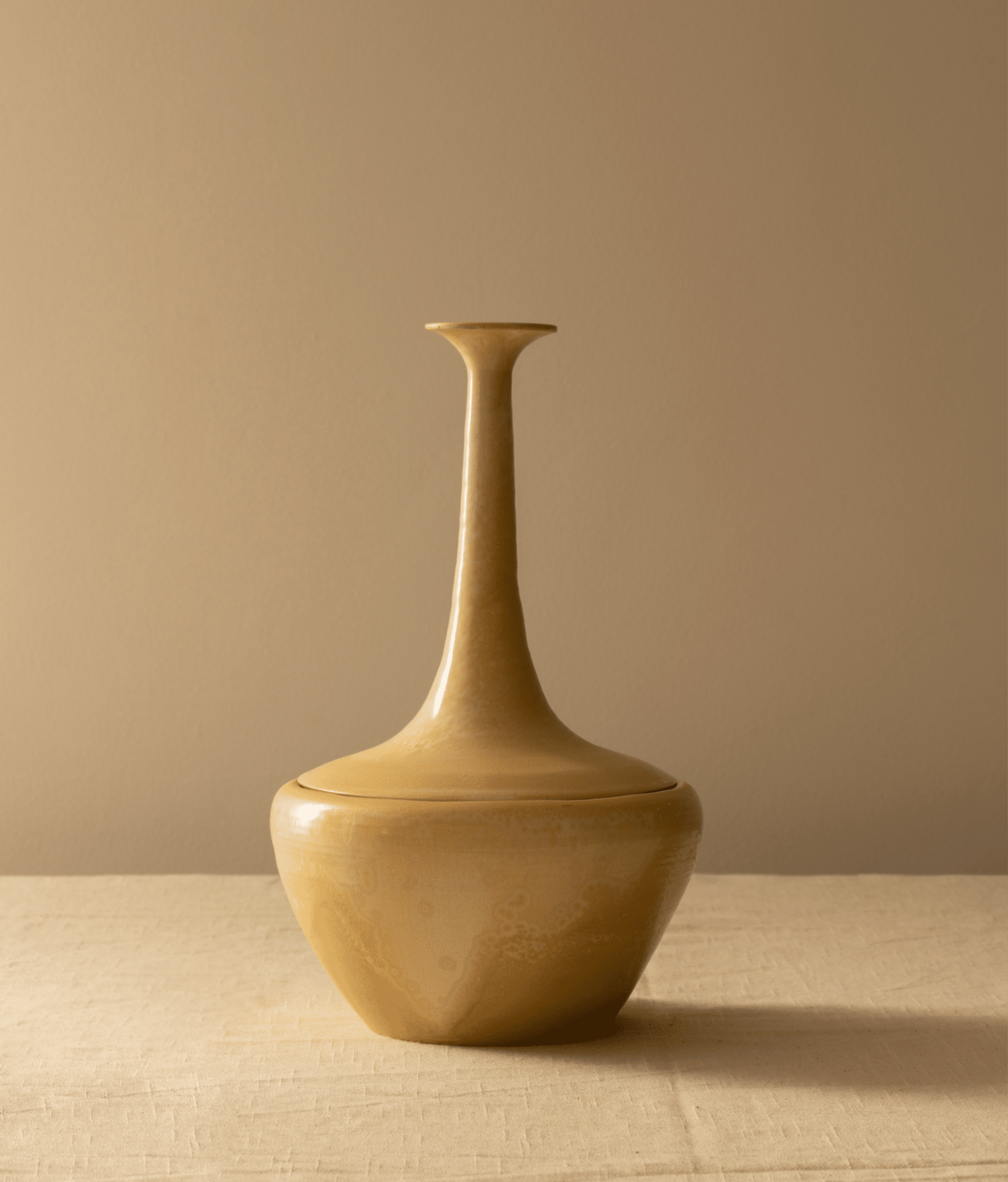 A single, elegant beige ceramic Two-Piece Pot with a slim neck and round base, featuring hand-painted floral details, stands on a textured beige cloth against a matching beige background.