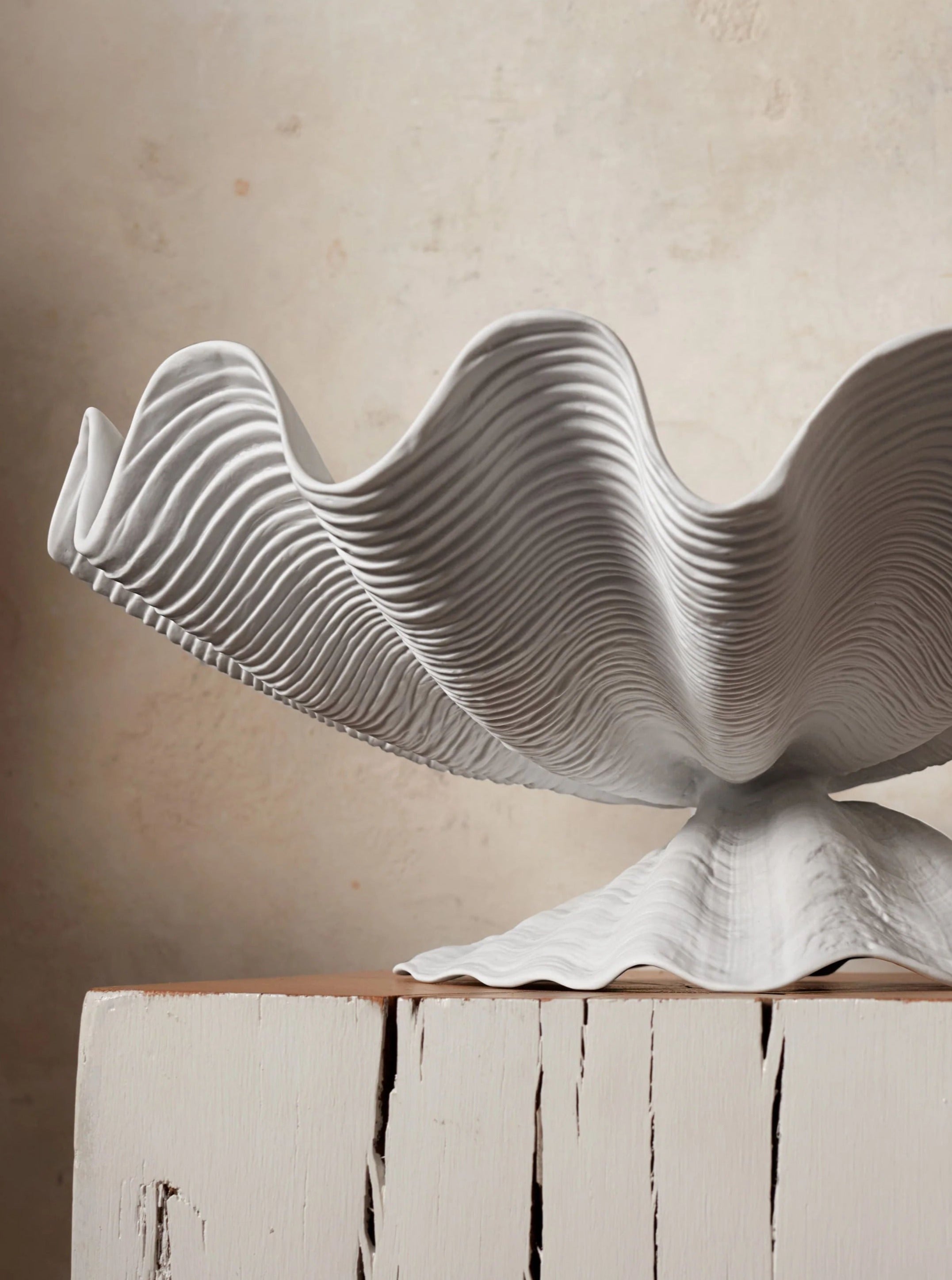 A sculptural Neptune Bowl Large by L'objet featuring undulating, layered waves, displayed on a time-worn, white painted wooden crate against a neutral background.