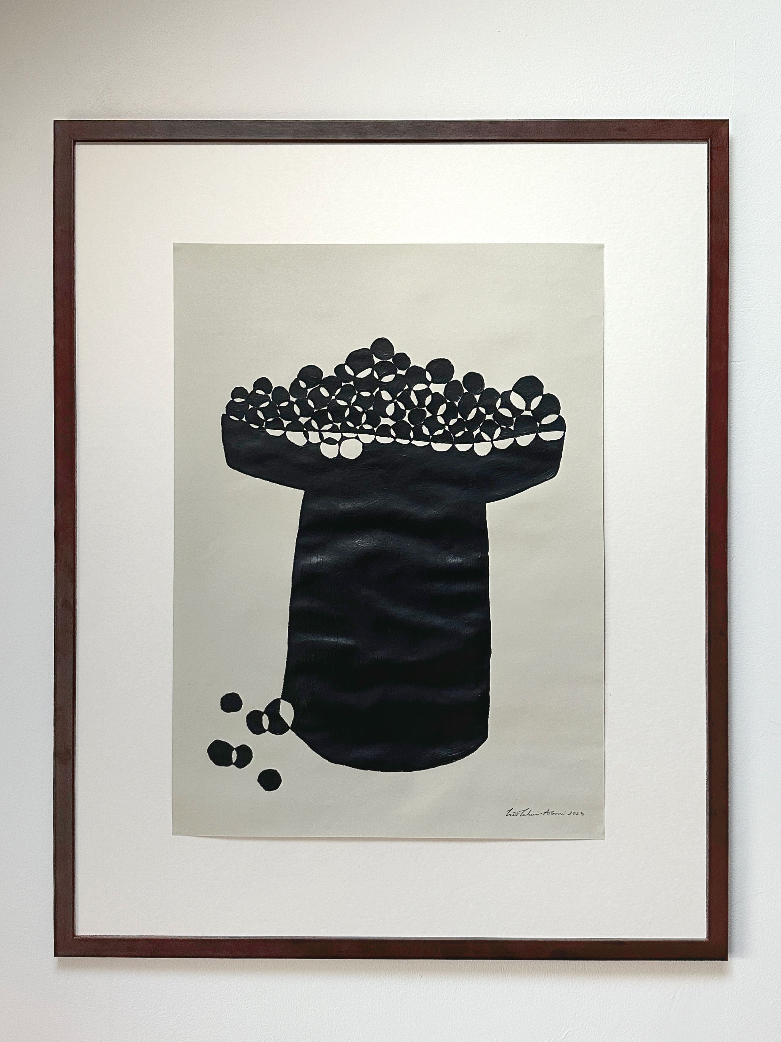 A framed abstract black and white artwork depicting Les Tomates Cerises, a cylindrical shape covered with rounded forms, possibly stones, positioned on a white background, signed at the bottom as "Les Tomates cerises" by Inès Tahiri-Alaoui.