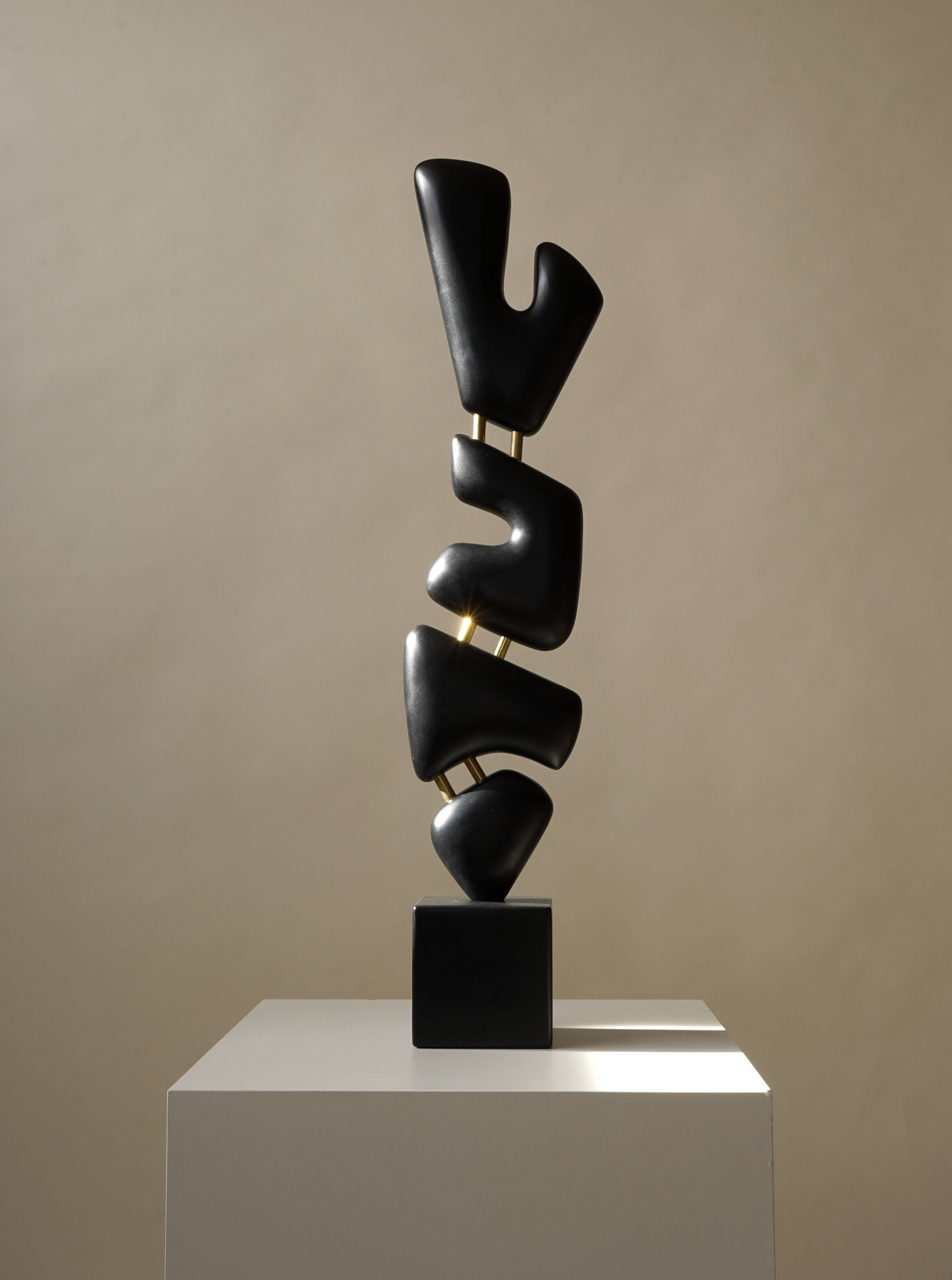 The Urbmon 116 Sculpture by Chandler McLellan is a modern, minimalist piece with handcrafted, smooth abstract dark forms stacked vertically on a pedestal, casting subtle shadows on a neutral backdrop.