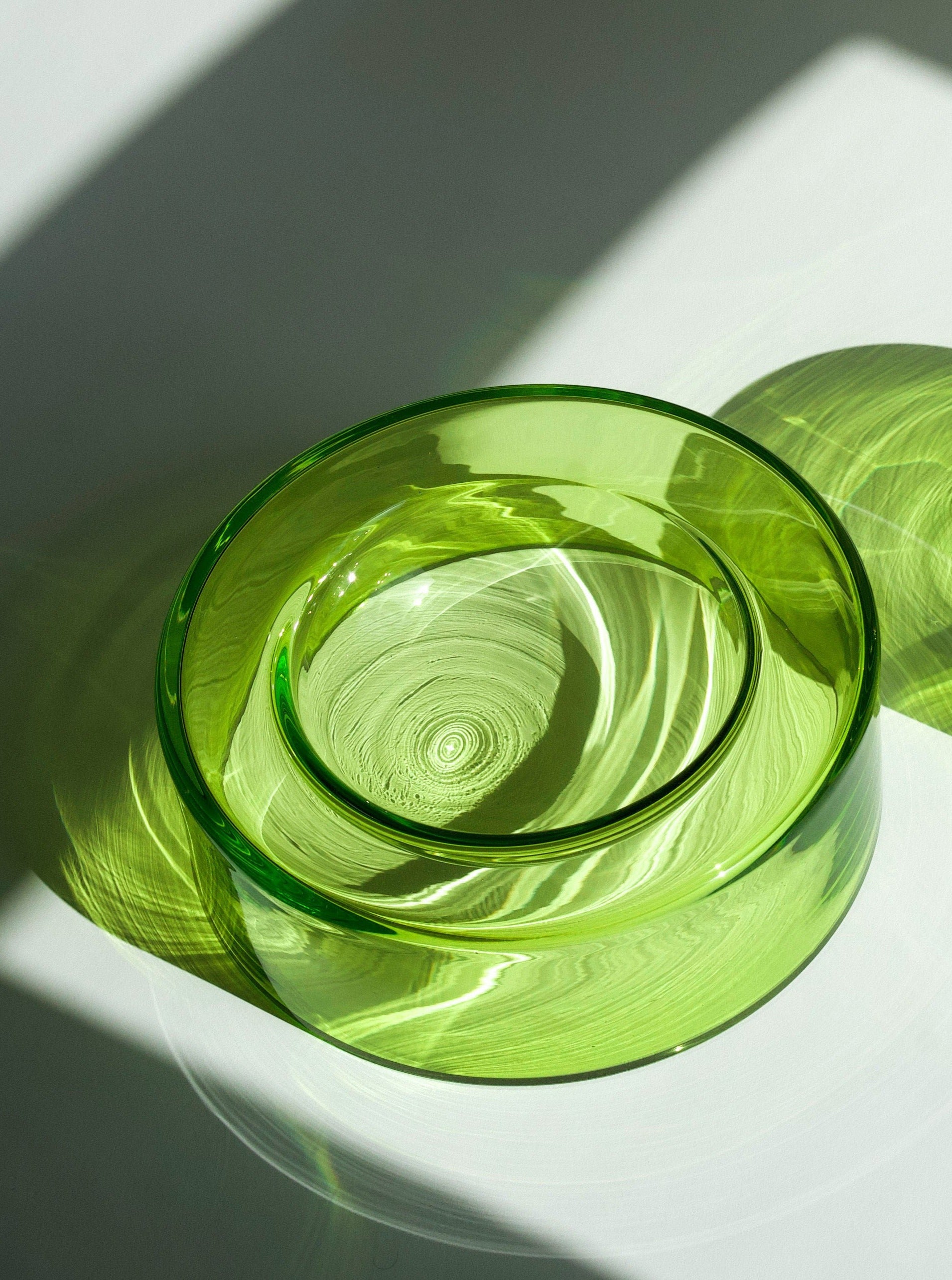 Two Wet Bowl - Medium Lime handcrafted glass bowls stacked inside each other, casting intricate shadow patterns on a sunlit white surface by Ursula Futura.