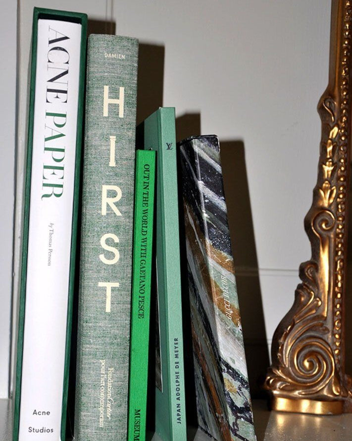Four vertically arranged Maison Plage interior design books with varying cover designs resting between a decorative golden frame on the right and a white background. The titles show eclectic themes from art to fashion campaigns.