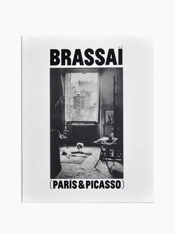 Book cover for "Brassai: Paris & Picasso" by Maison Plage featuring a black and white photograph of an art-filled room with a framed Picasso artwork and scattered objects, conveying a vintage Parisian aesthetic.