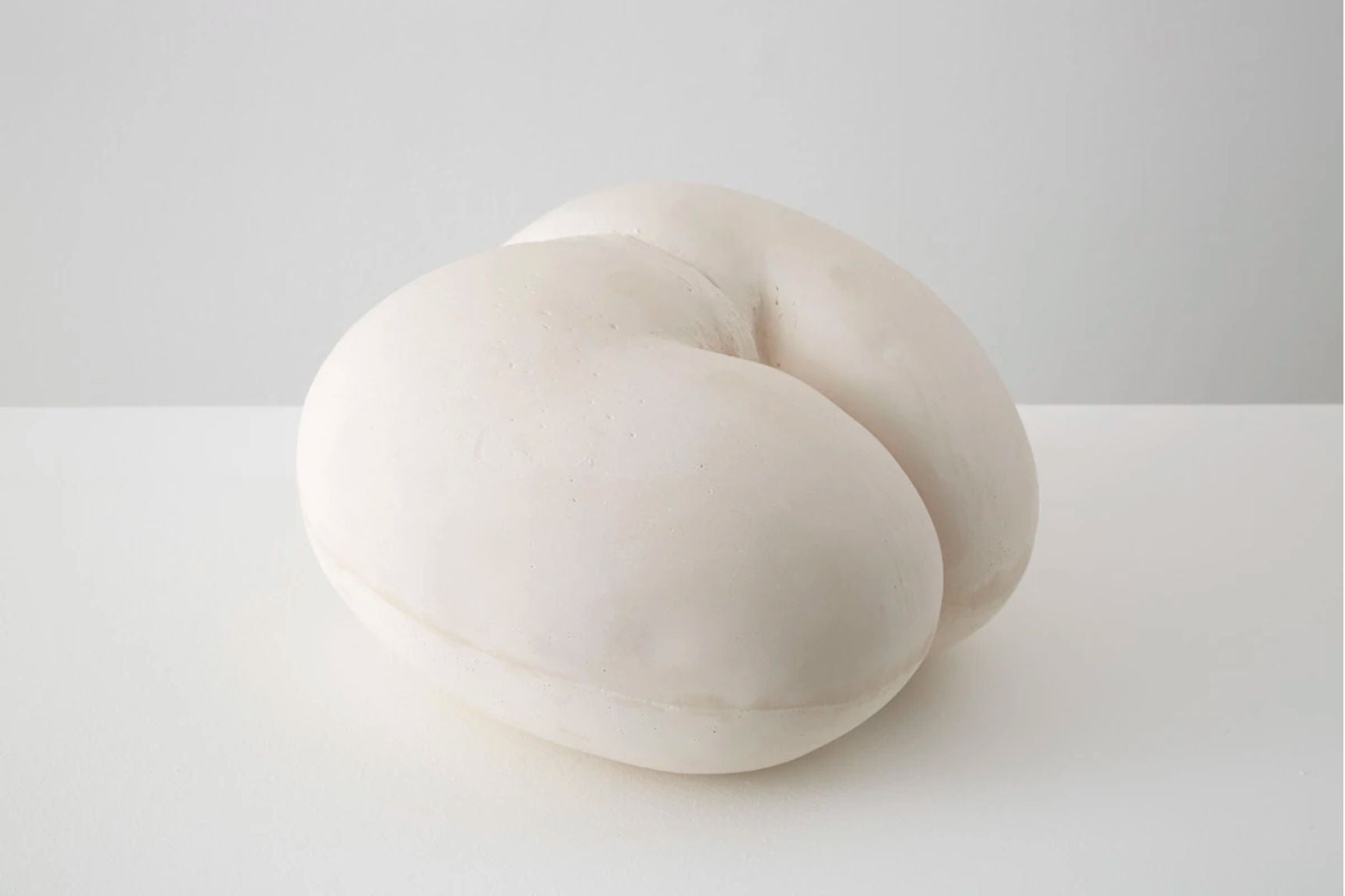 A smooth, white, plaster sculpture resembling two interconnected forms from the Double Cream series by Alba Hodsoll Studio on a plain background, evoking a serene and minimalist aesthetic.