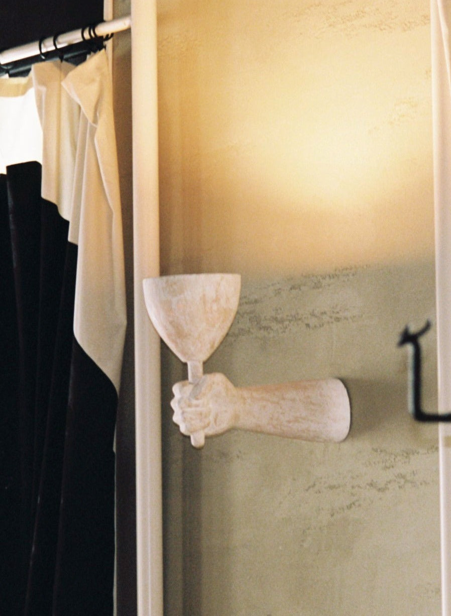A Dracula Wall Scone Composite mounted on a wall, holding a shallow bowl, with soft lighting reflecting off beige wall surfaces, evoking an elegant and artistic ambiance by Rooms Studio.