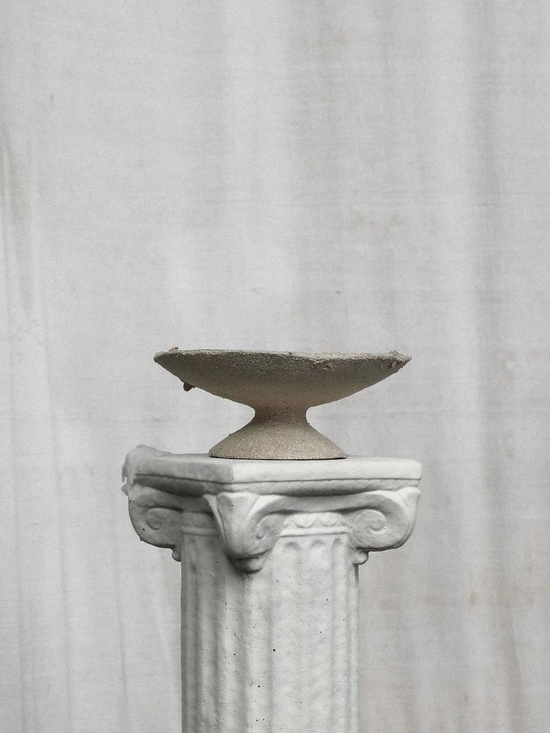 The Frutera Decorative Bowl by Emma Lindegaard Studio, featuring textural beauty, sits on a textured, ornate white pedestal against a plain white backdrop.