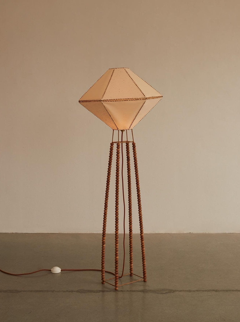 The Lana Launay USO Floor Lamp showcases an elegantly crafted diamond-shaped beige shade made from eco-friendly textiles, supported by four sleek metal rods.