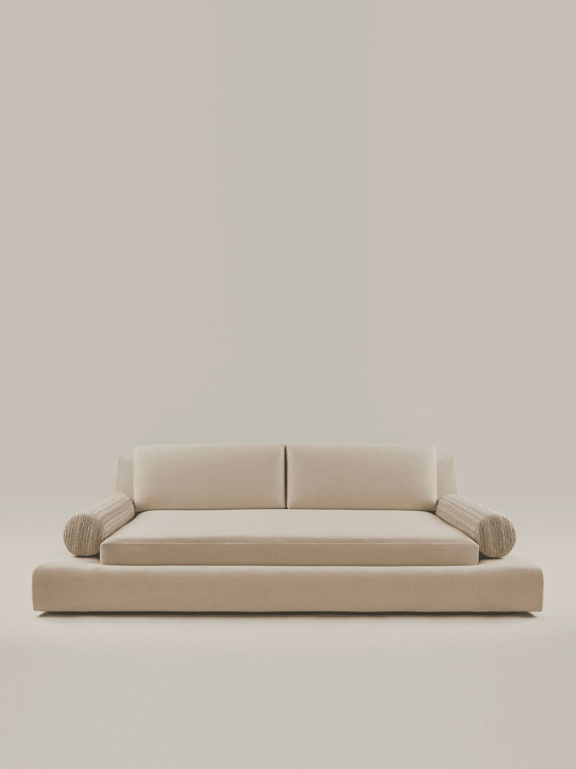 The "Podium" Sofa by HAUVETTE & MADANI is a minimalist seventies-inspired piece in washable cotton velvet, featuring a beige hue with two back cushions and cylindrical side cushions on a neutral background.