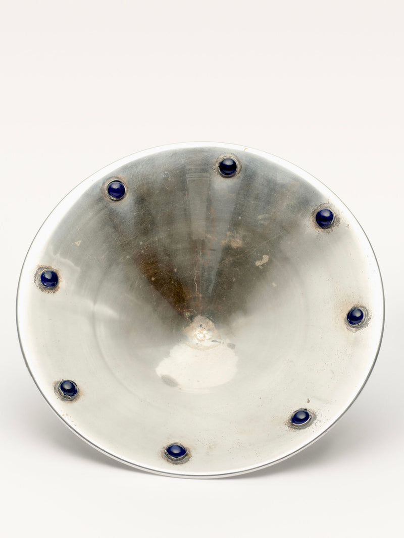 The Galerie MLS Silver Plated Bowl with Blue Stones features an elegant design with a reflective surface and small blue stones evenly spaced around the inner rim, adding a decorative touch to its metallic finish, capturing attention even in used condition.