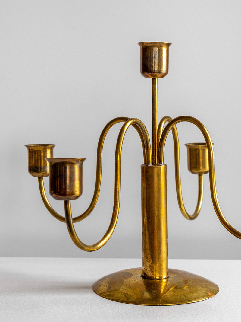 The Spigel Mid-Century Brass Candelabras feature a vintage design with a central stem and four elegantly arched arms, each supporting a candle cup. The minimalist and symmetrical structure, subtly accented with patina, boasts a polished surface that beautifully reflects light. Photographed against a plain background, this timeless piece effortlessly elevates any space.