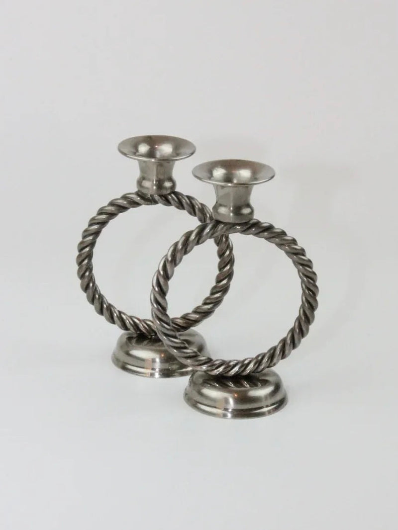 Two Mental Candle Holders by Boga Avante Shop featuring a twisted rope design forming circular holders are shown on a plain background. The bases are round and stable, with wide openings at the top to hold candles. The overall design is timeless, exuding a classic and sophisticated look that's both elegant and symmetrical.