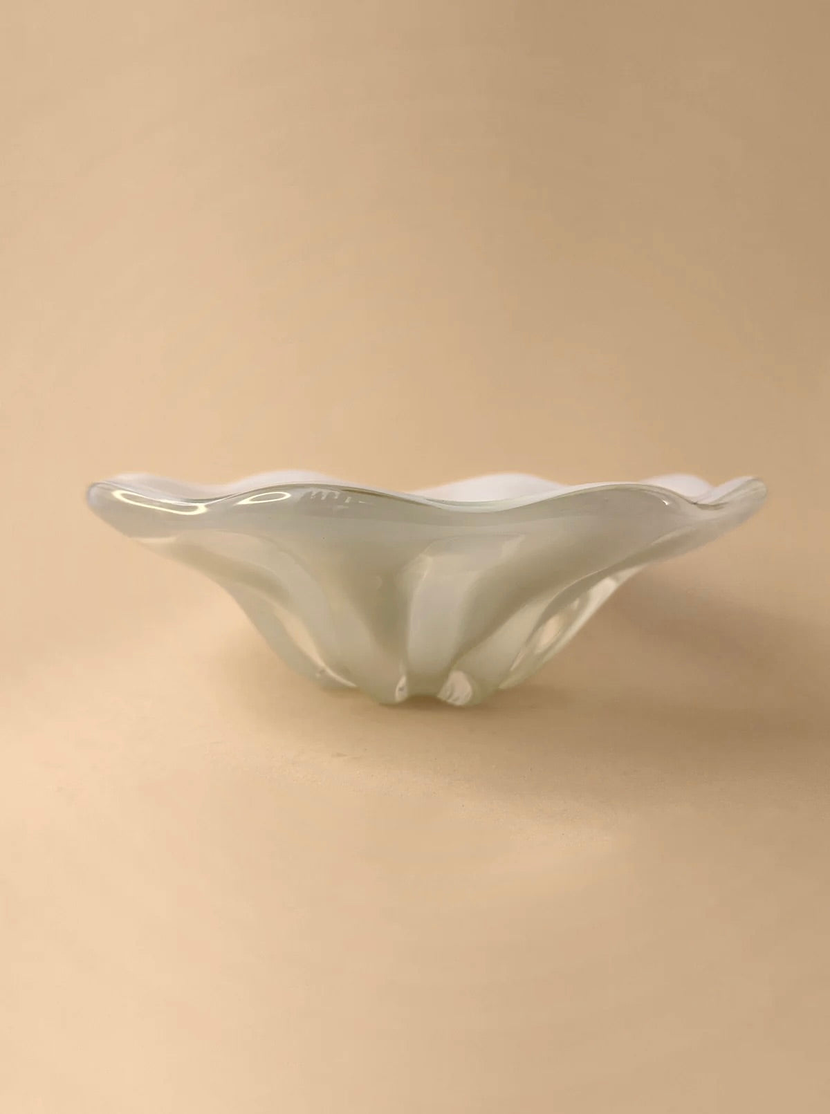 A Mid Century Murano Milky Bowl by Barovier & Toso from Dodo Vintage, in a translucent light green hue with a fluted, wavy rim, sits on a neutral beige surface. Crafted using the intricate Seguso technique, it features a smooth and elegant design. The overall appearance is delicate and artistic.