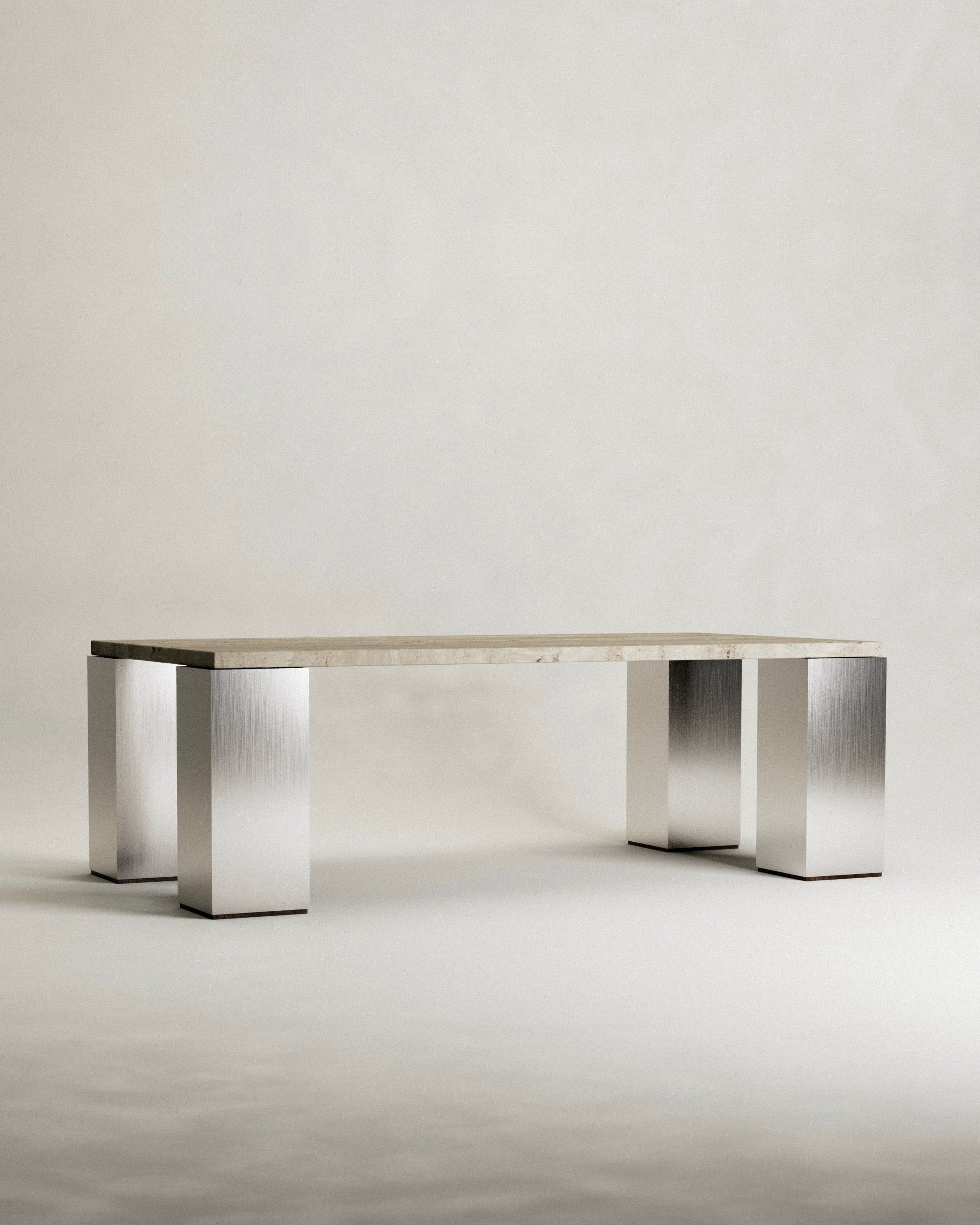 The 'Fragua' Dining Table by Siete Studio features a rectangular beige top and four metallic legs. This modern, minimalist piece highlights metallurgical craftsmanship with brushed metal textures on the legs, set against a plain design backdrop.