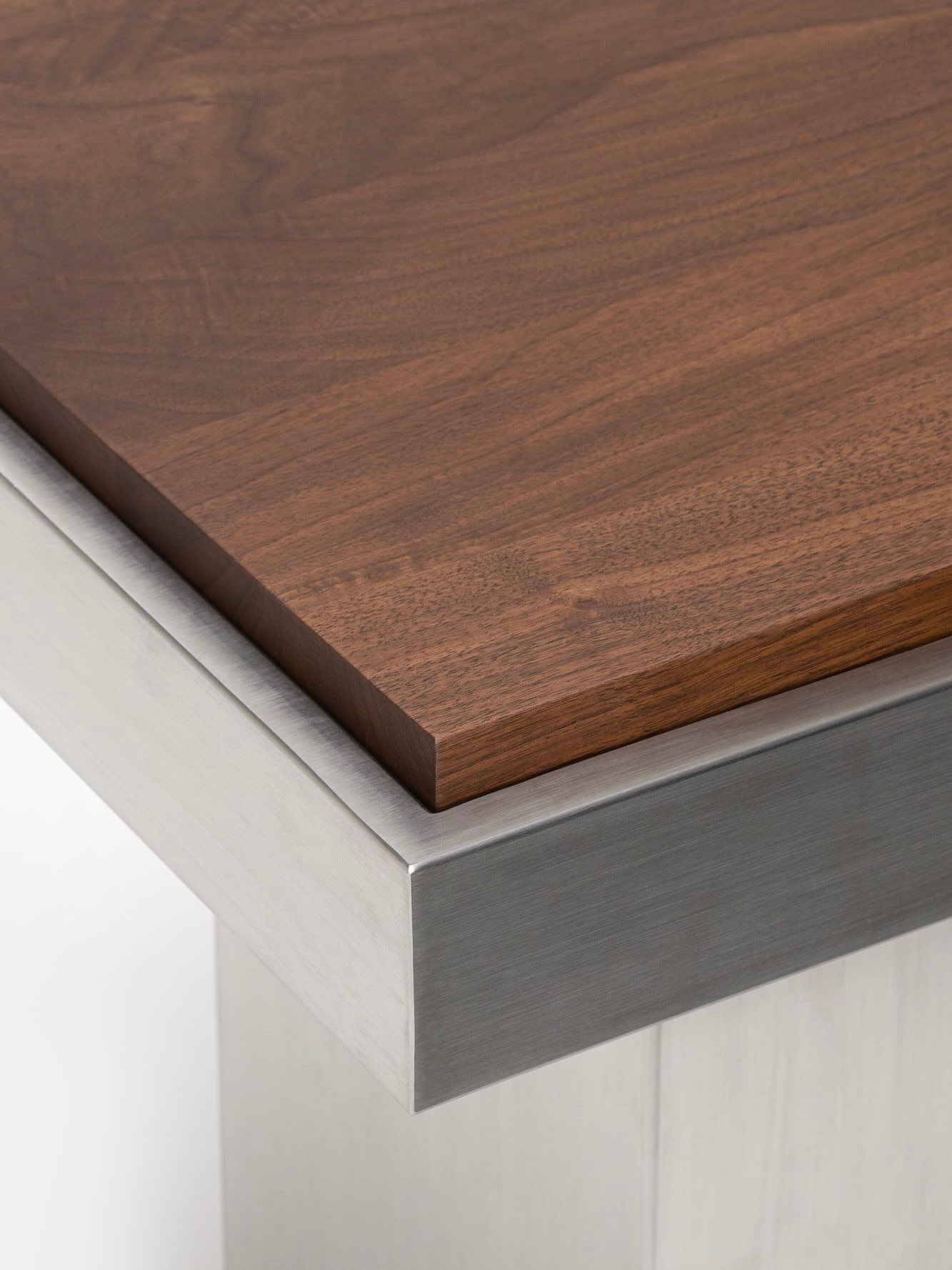 Close-up of the Console Table 02 corner by Studio Vraco, featuring a smooth, rich brown wooden top paired with a brushed stainless steel frame. The contrast between the warm wood grain and the sleek metal evokes the modern elegance characteristic of Bauhaus furniture.