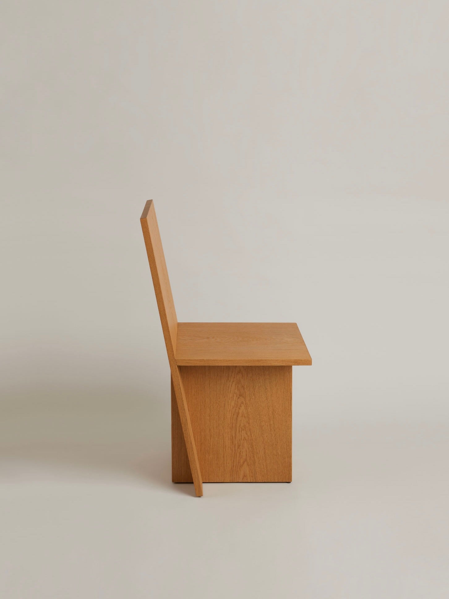 A side view of the "La Coupe" modular chair by HAUVETTE & MADANI, crafted from brushed oak, is set against a plain background. This minimalist chair highlights a flat seat and backrest, both connected at right angles to its solid base.