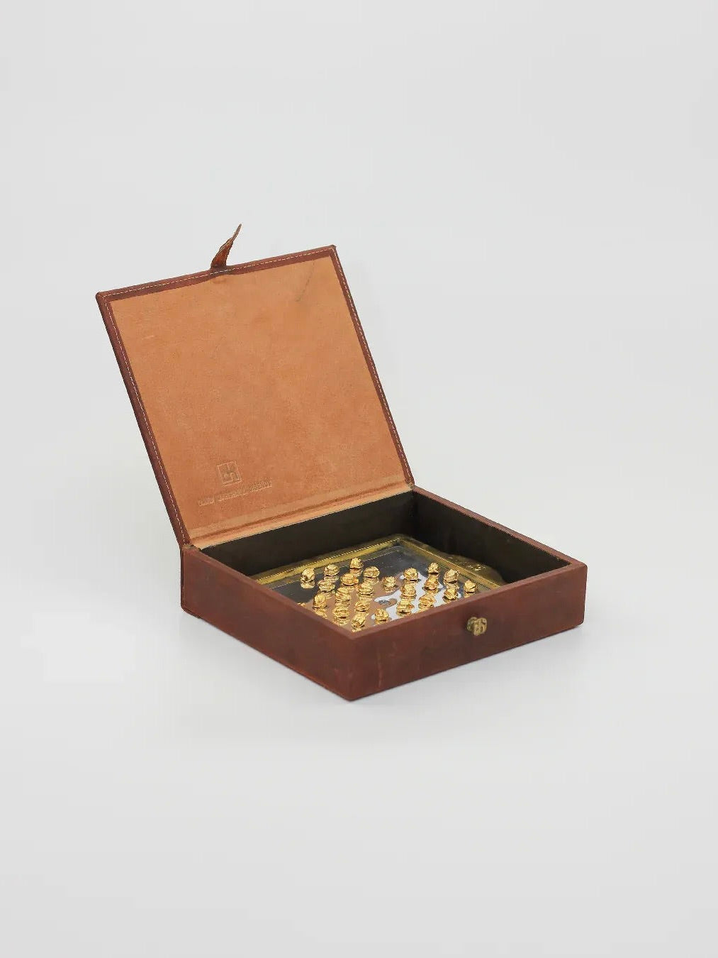 A luxurious English Solitaire chess set from Boga Avante Shop is showcased in an open brown velvet-lined box. Designed by David Marshall, the set features intricately crafted gold and silver pieces with brass and aluminum accents, all highlighted against a plain gray background to evoke vintage charm.