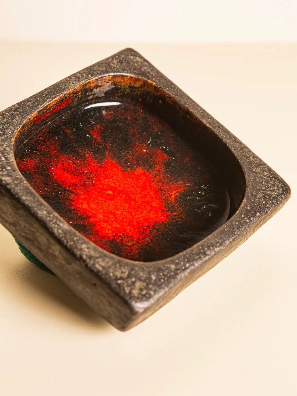 The "60's Square Ceramic Tray" by Jan Van Erp, offered by Treaptyque, presents a rustic appeal with its black glaze and striking red splash at the center. Much like a decorative masterpiece, this distinctive tray adds character to any plain setting, reminiscent of an elegant square ceramic storage caddy.