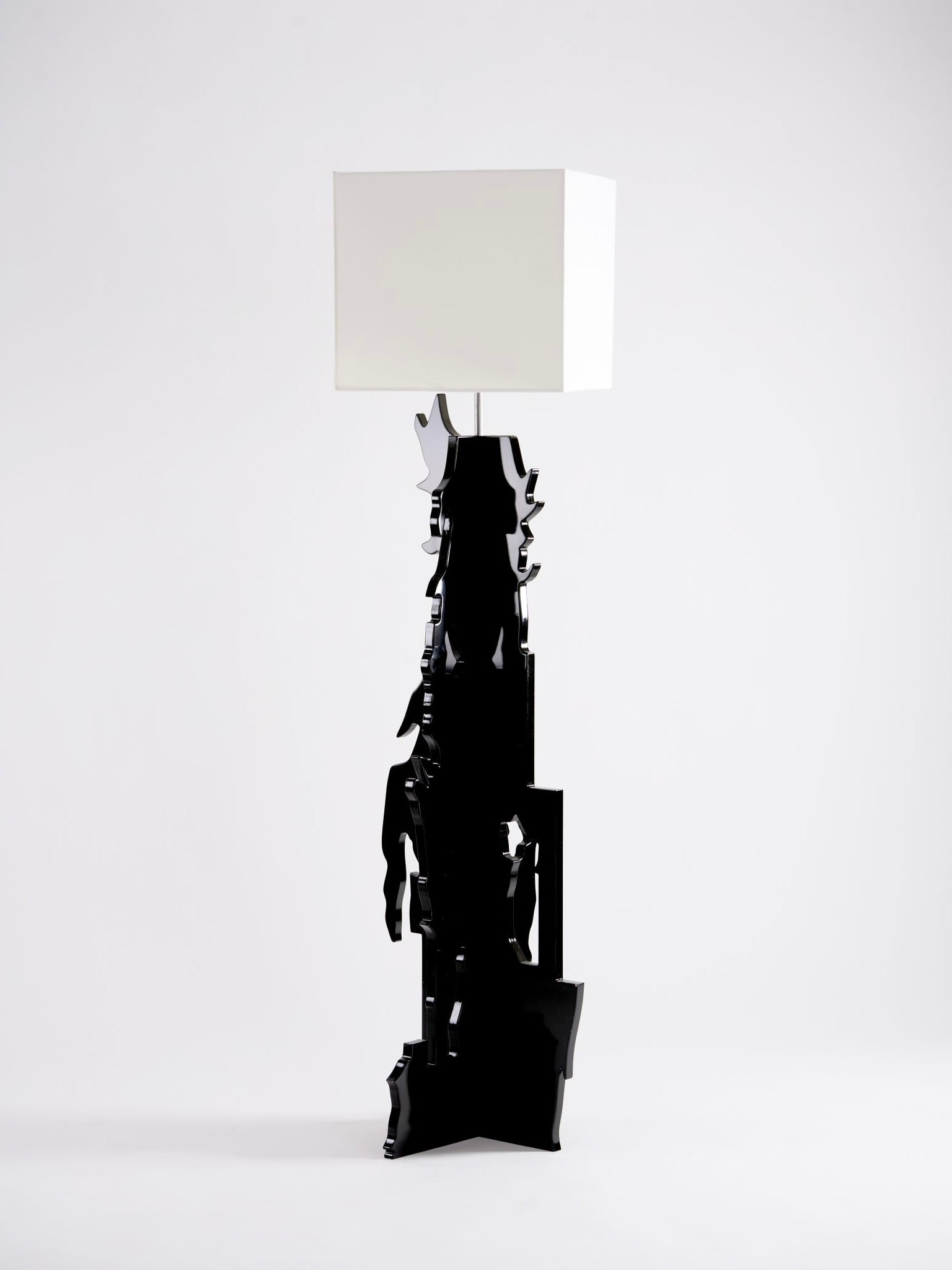 The Ochoa Rocabert "The Beast" Floor Lamp showcases a sleek, black sculptural base with modern, abstract designs similar to a Rorschach test, complemented by a white square lampshade against a simple white backdrop.