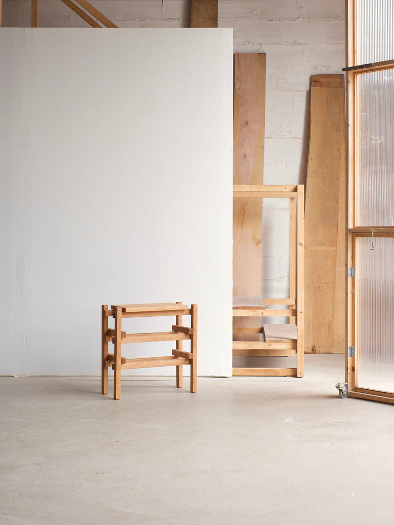 A Stool Palma by malva is placed in an airy, modern room with white and wooden walls. The room features natural light from large windows and has some wooden boards leaning against the walls in the background. The space beautifully blends industrial durability with cozy charm.