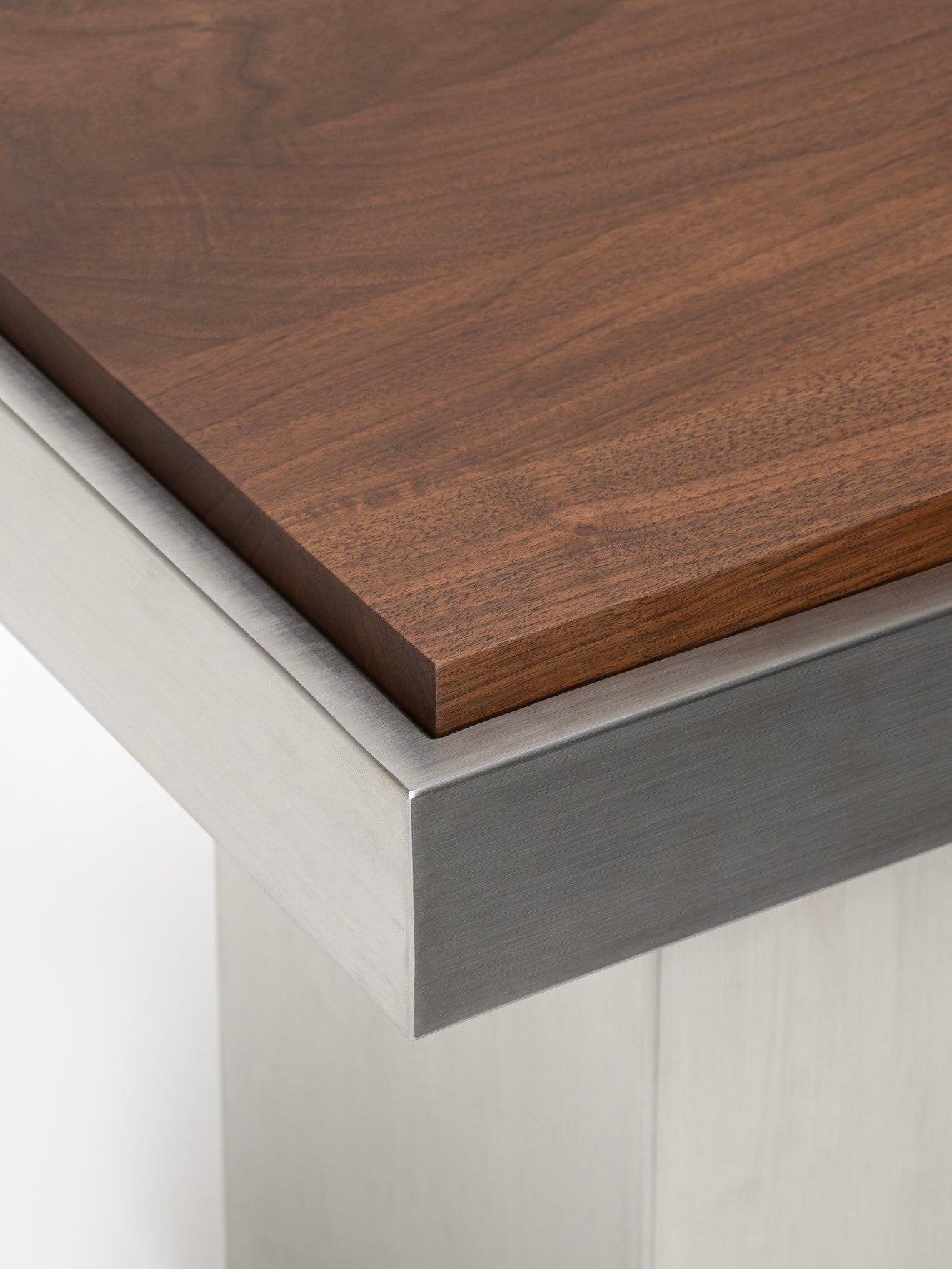 A close-up of the Studio Vraco Console Table 01 showcases its polished metal base and dark wooden top with a smooth finish. The image accentuates the contrast between the brushed stainless steel and warm wood textures, capturing a touch of Bauhaus furniture elegance.