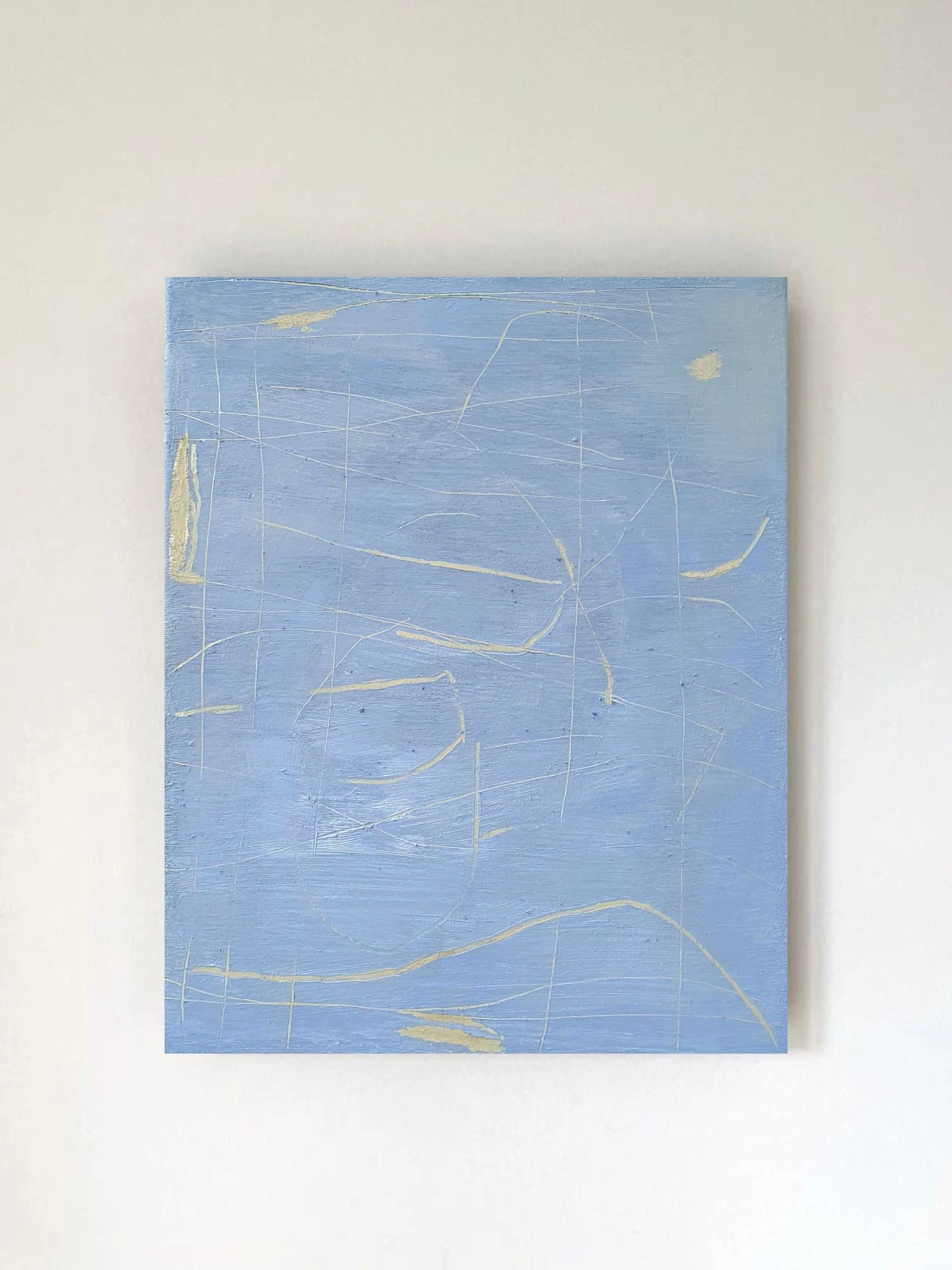 The Unsaid" painting by Yeliza Gevorgyan adorns a light wall. This large abstract canvas, mainly blue with subtle white and pale yellow lines, exudes a sense of ancient worlds through its textured finish.