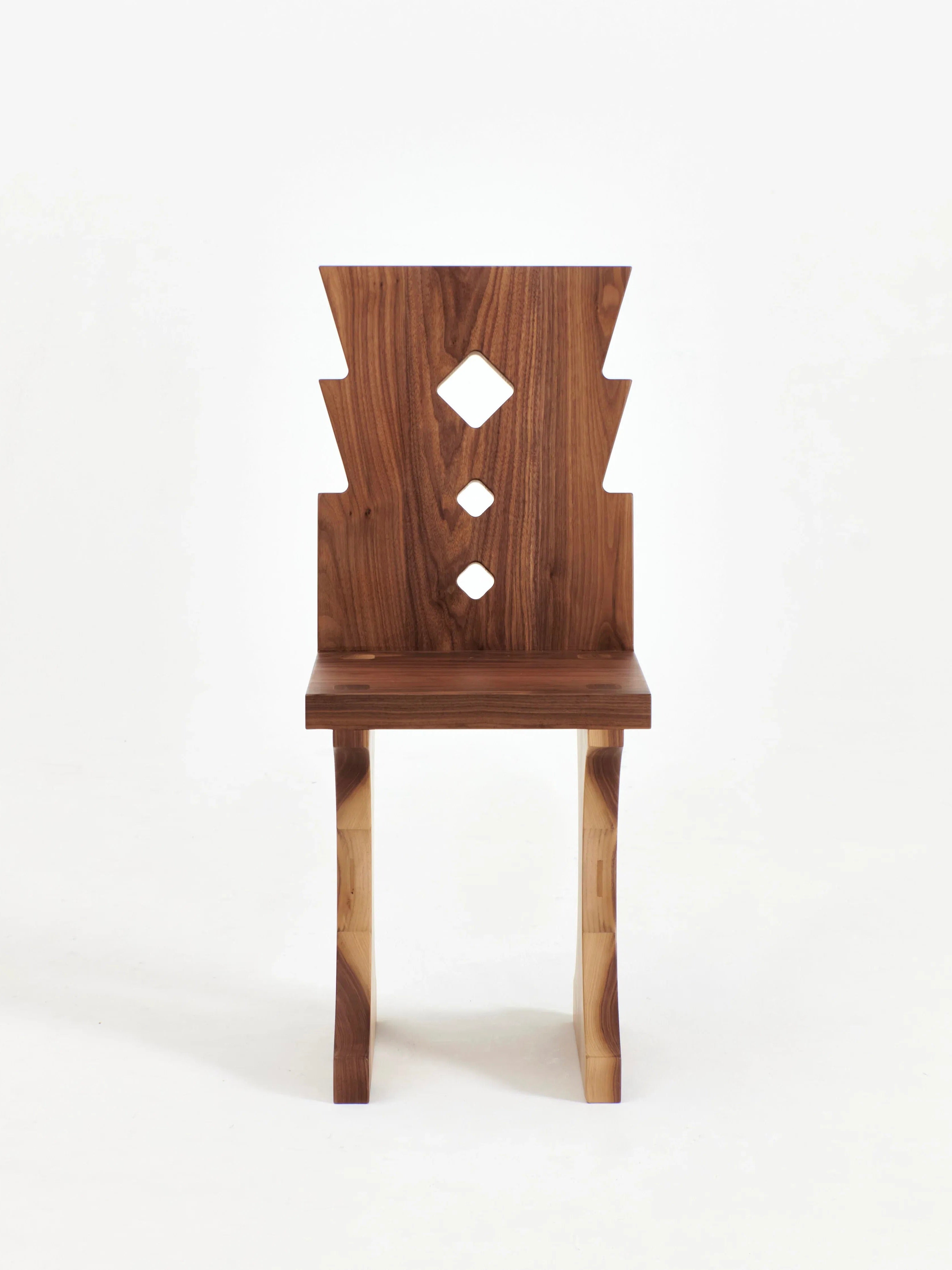 The Portugal Chair No 6 by Project 213A is a hand-carved walnut chair featuring a tall backrest with three vertically arranged diamond-shaped cutouts in varying sizes. Its angular edges offer a modern, geometric aesthetic, while the chair legs boast a simple and sturdy design. This elegant piece is showcased against a white background.