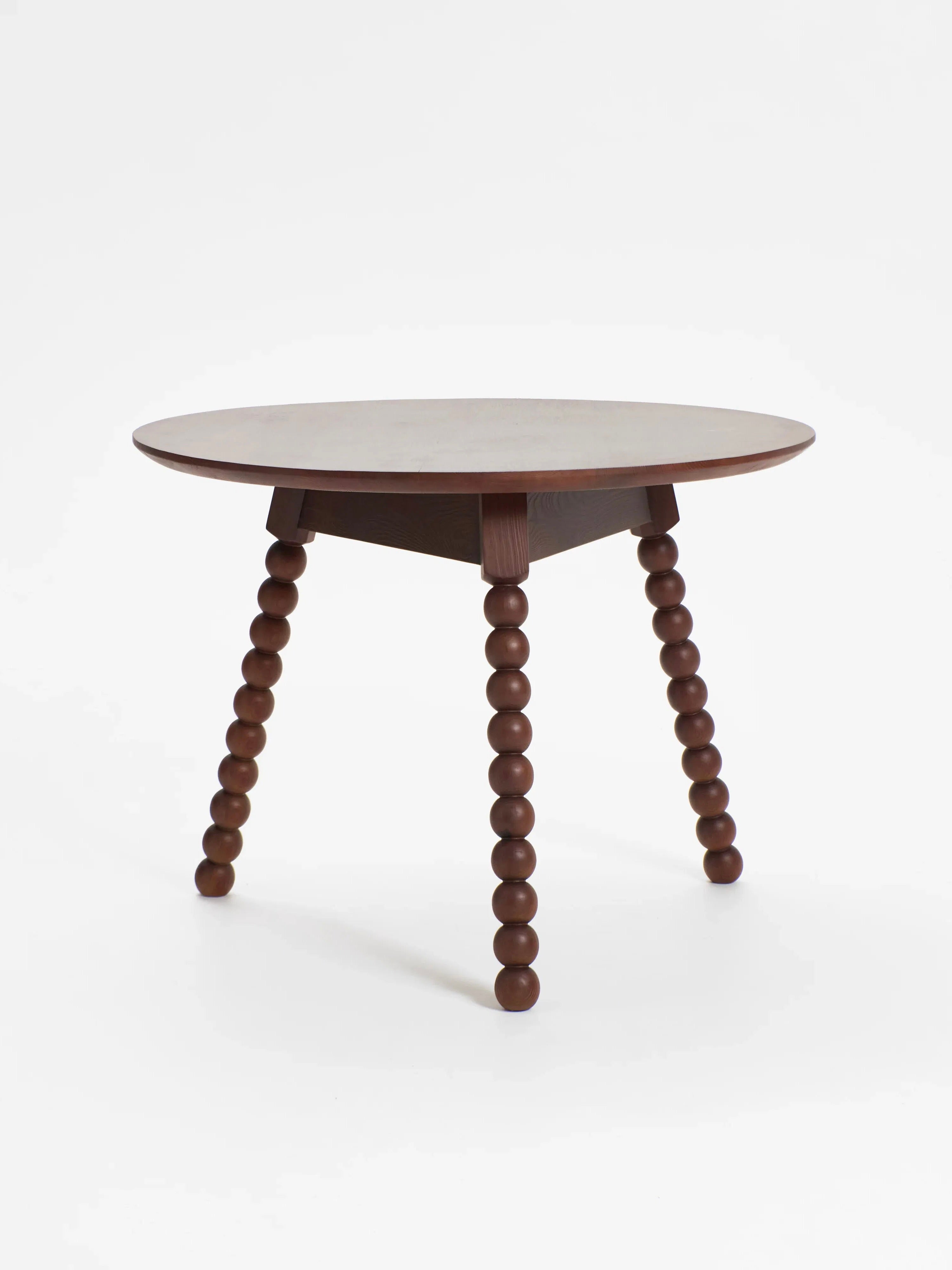 The 'Bolha' Table by Project 213A features a smooth, round solid wood top and three legs made from stacked spheres with intricate detailing, all in a dark, rich finish that contrasts elegantly against a plain white background.