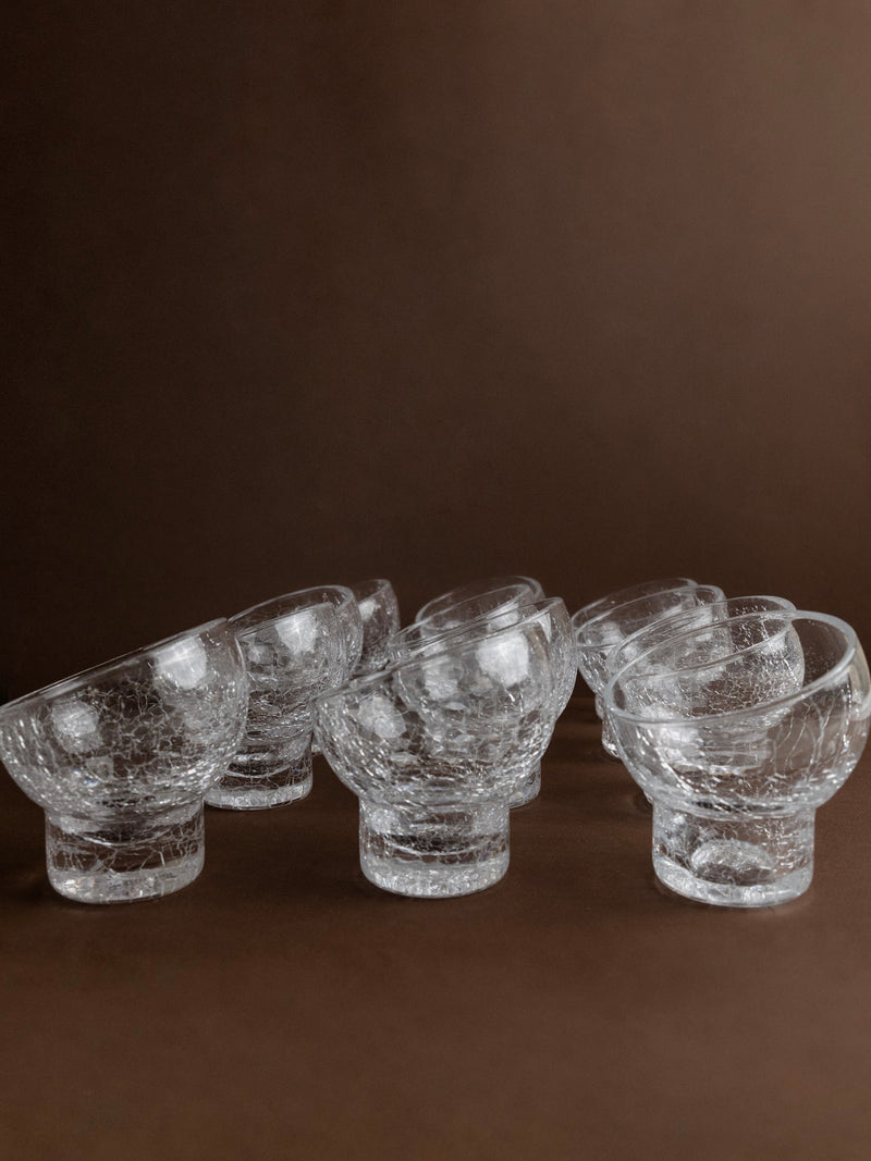 A set of 12 wine and cocktail glasses from Bottega Jacobs, Italy 1970s, is artfully arranged to form intricate patterns against a brown backdrop.