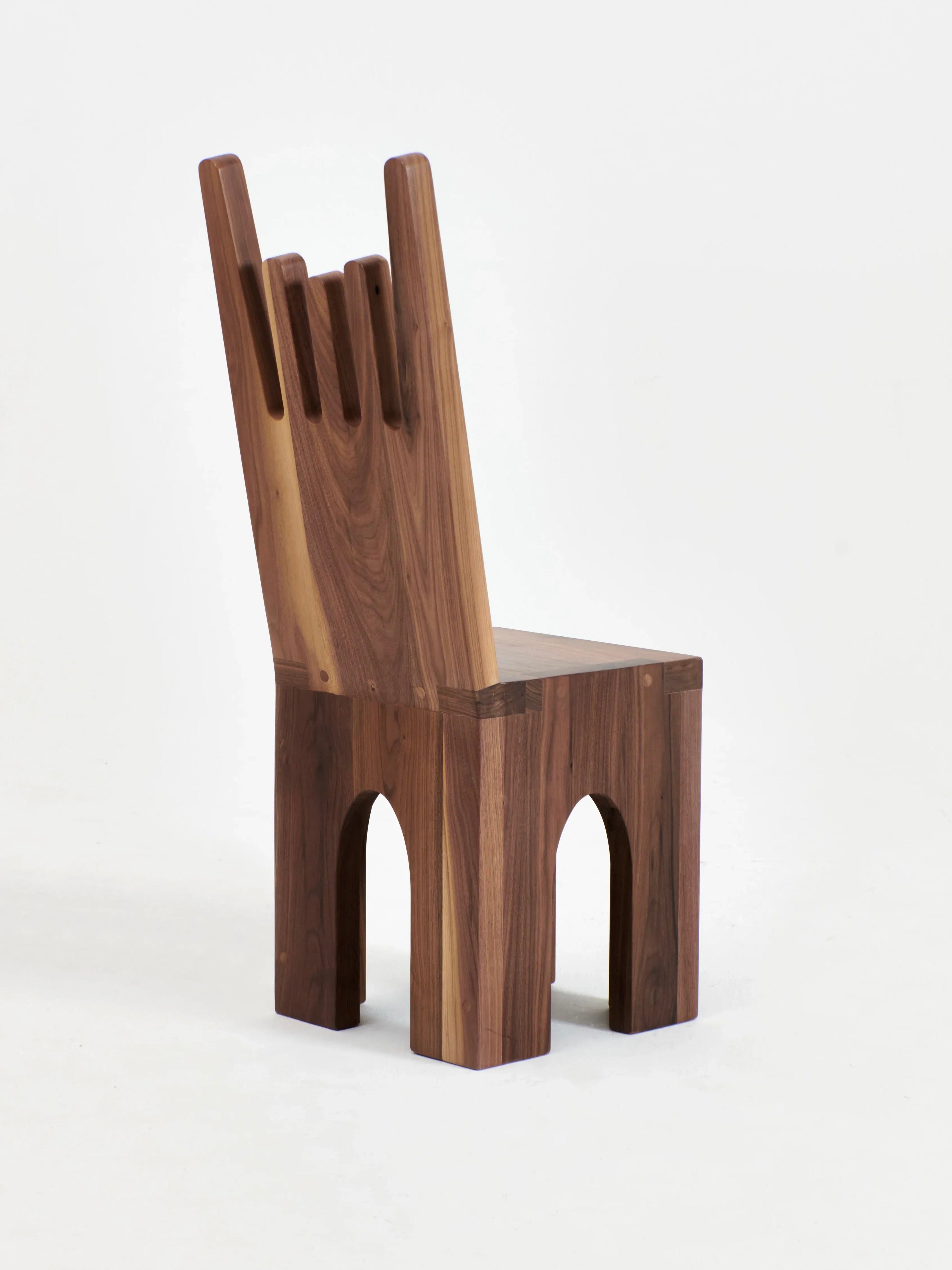 The Portugal Chair No 5 by Project 213A is a wooden marvel crafted from solid walnut, featuring a unique, graphic-shaped backrest with tall, rectangular cutouts. Its chunky legs boast arch-shaped cutouts on the front and sides, lending it a modern and architectural appeal.