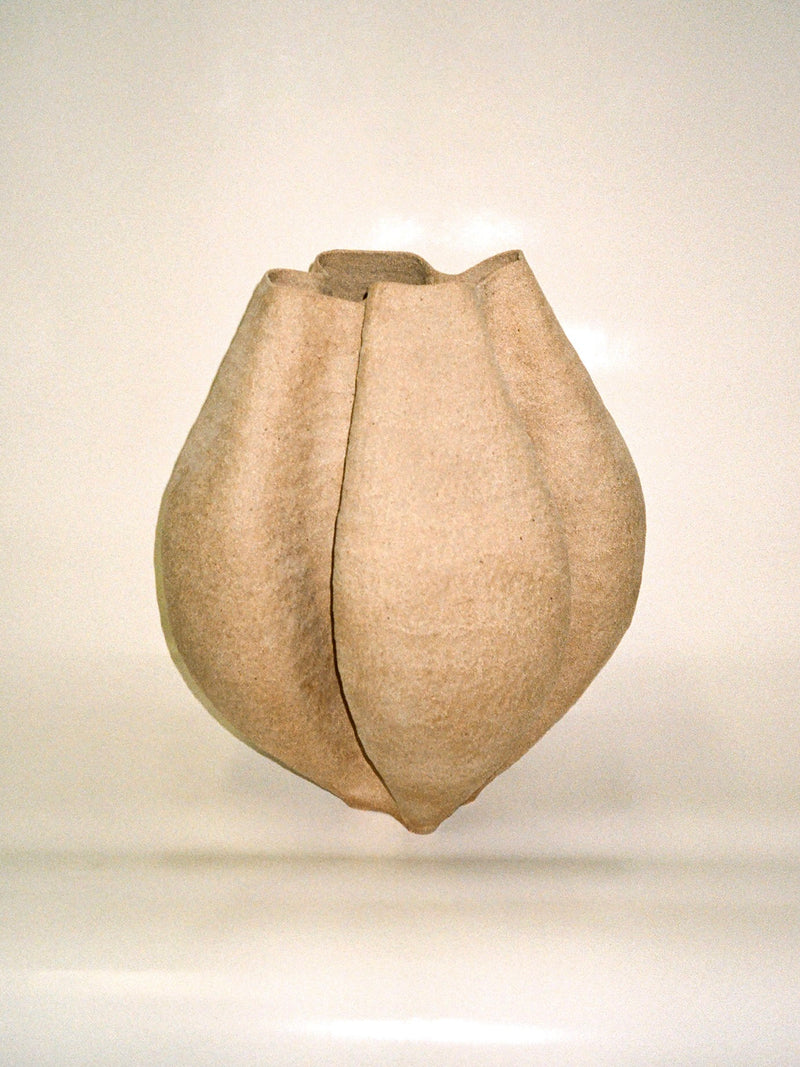 The Growing Vase n.3 by Aiste Bagdonaite is a beige, textured stoneware vase with soft vertical ridges and a bulbous, flower-bud-inspired shape. Its small opening and organic form make it a unique statement piece for any space.