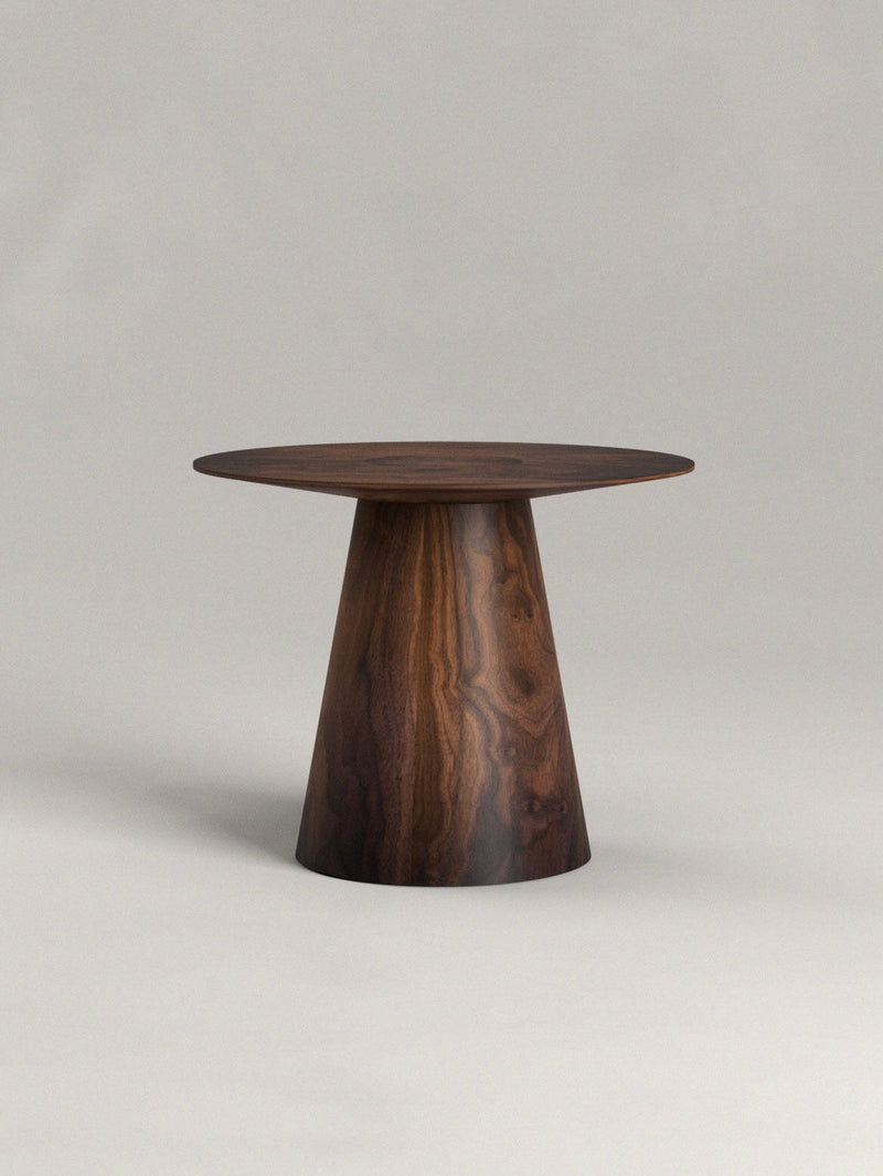 The Totem Side Table by Siete Studio stands against a plain gray background, featuring a small, round surface handcrafted from walnut with striking natural wood grain patterns on its conical base.